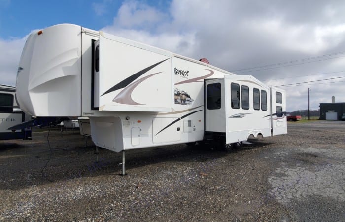 This white fifth-wheel RV rental offers ample space with its extended slide-outs, parked outdoors.. Forest River Cedar Creek Silverback 2012