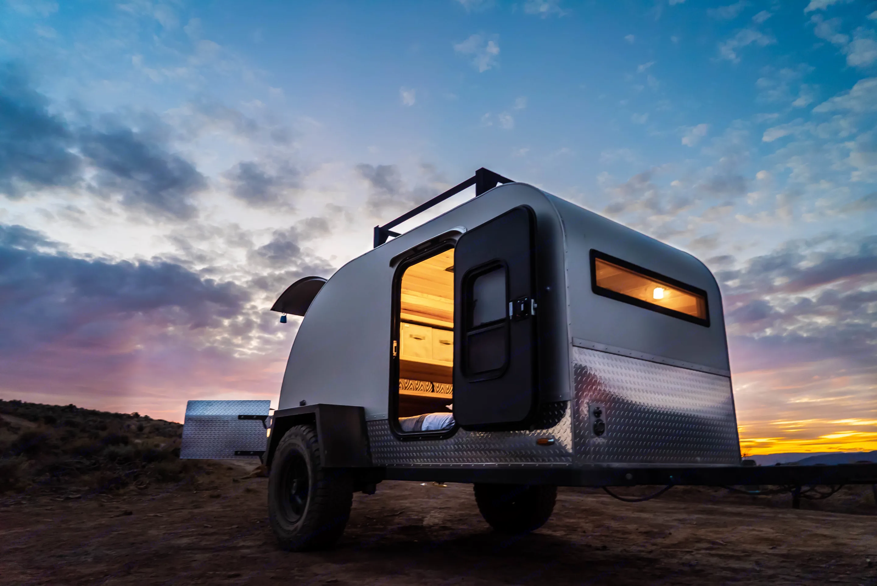 Teardrop camper at sunset, door open, interior light glowing. Perfect for an rv rental. PINNACLE Pinnacle Summit 2020