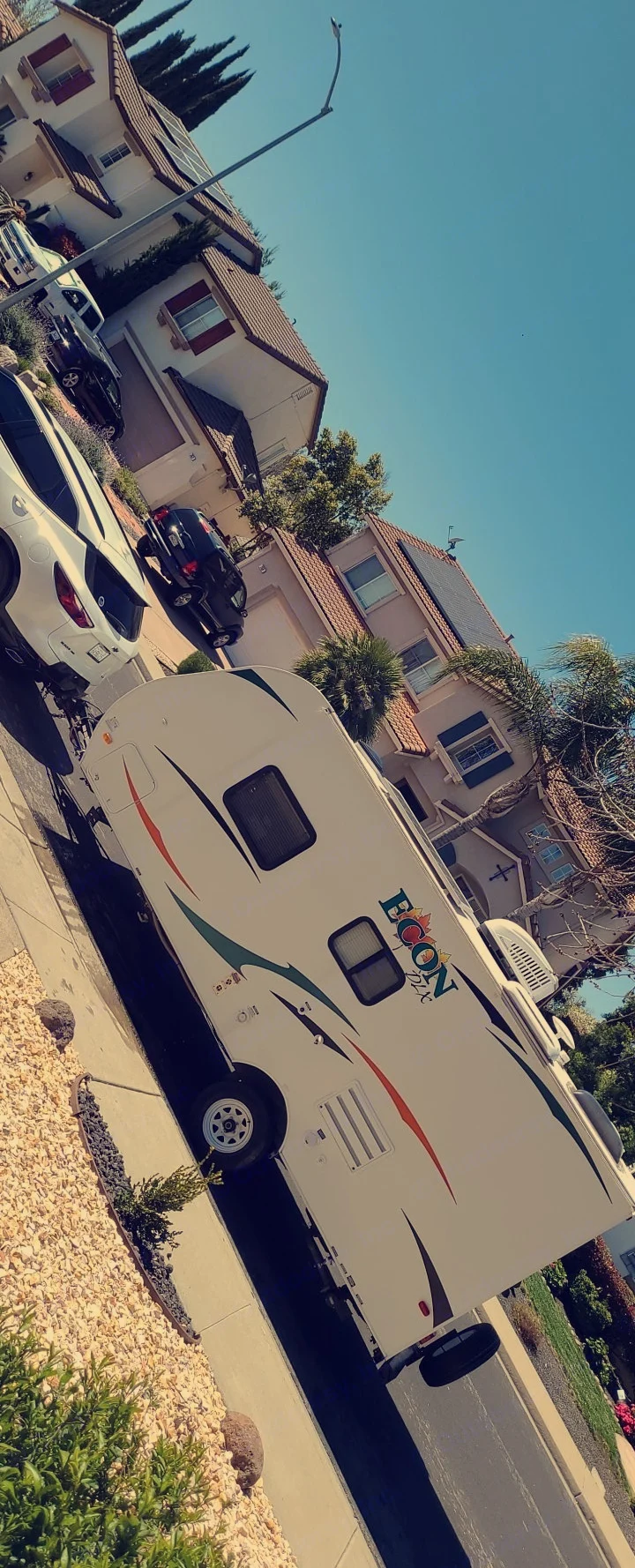 White "ECON DLX" travel trailer (RV rental) parked on a sunny residential street. Homes with solar panels line the road.. Pacific Coachworks Econ 2014