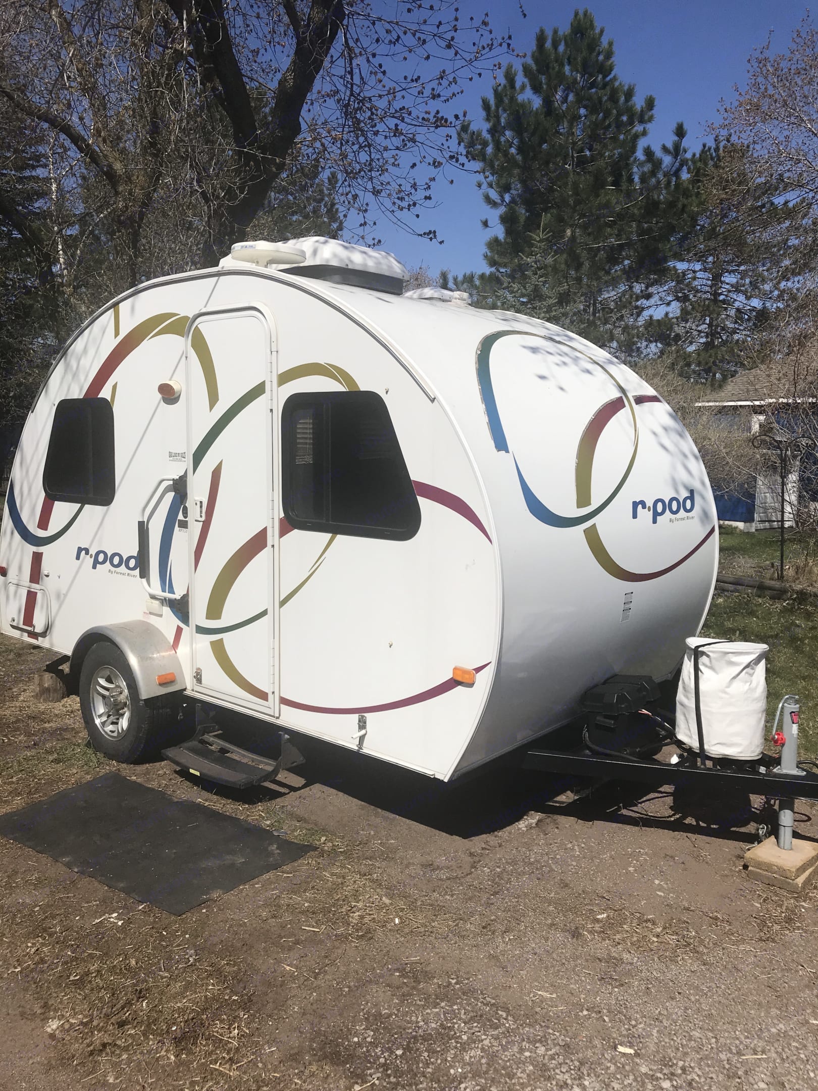 White r-pod teardrop RV rental, decorated with colorful swirls, parked outdoors on gravel. Perfect for camping adventures.. Forest River R-Pod 2010