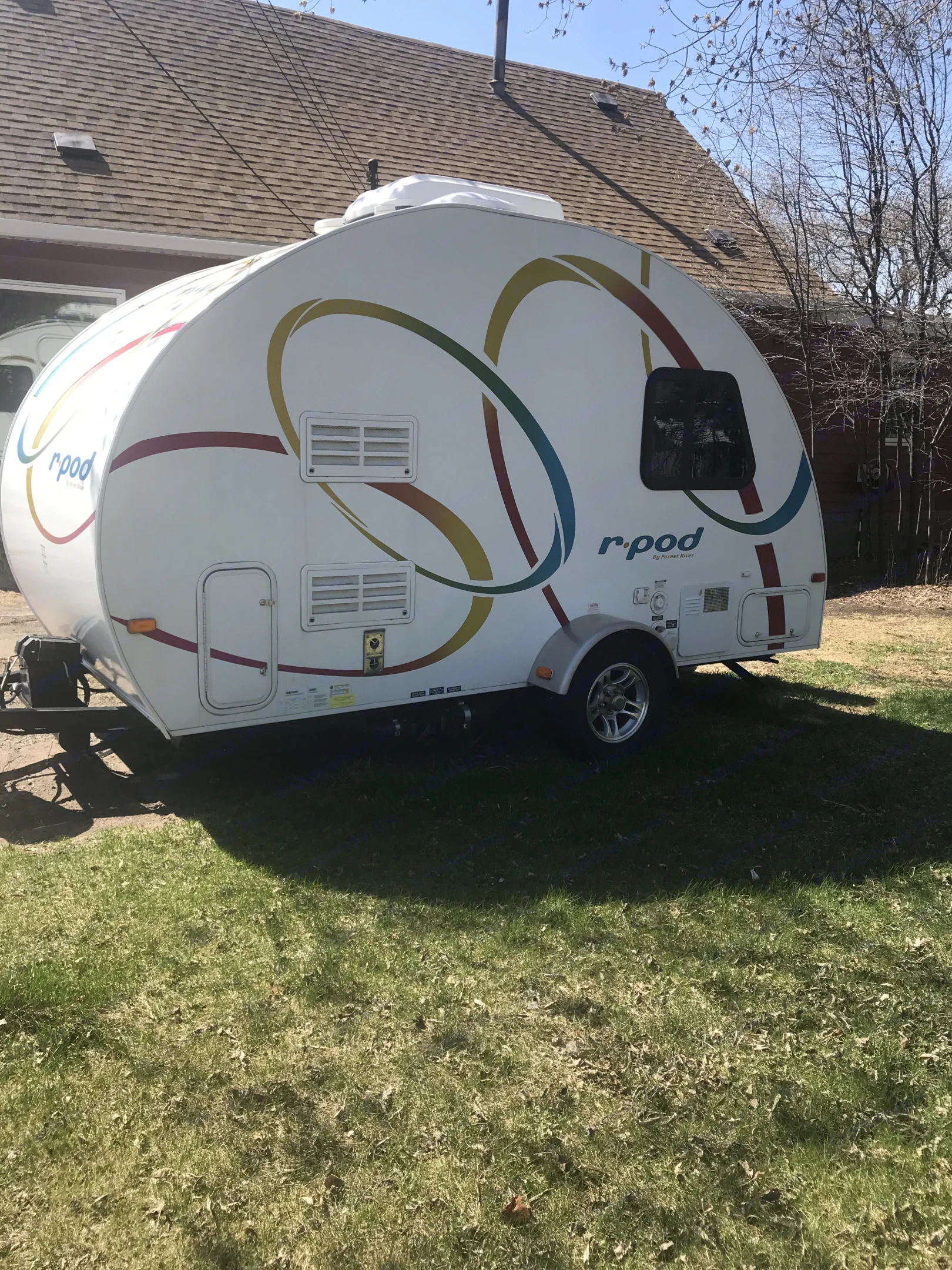 White r-pod travel trailer parked on grass. Ideal for RV rental adventures, featuring colorful ring decals on its side.. Forest River R-Pod 2010