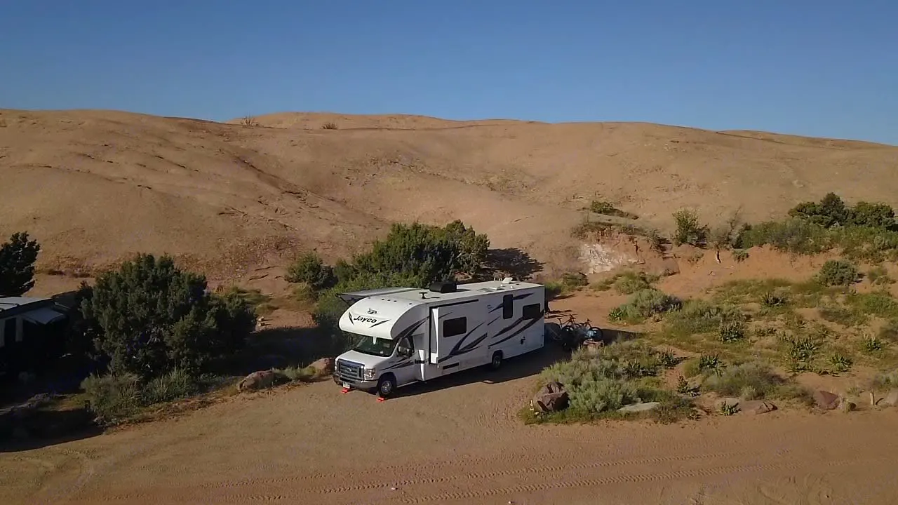 A white Jayco RV rental is parked at a scenic desert campsite with bikes, suggesting adventure travel and outdoor living.. Jayco Redhawk 2018