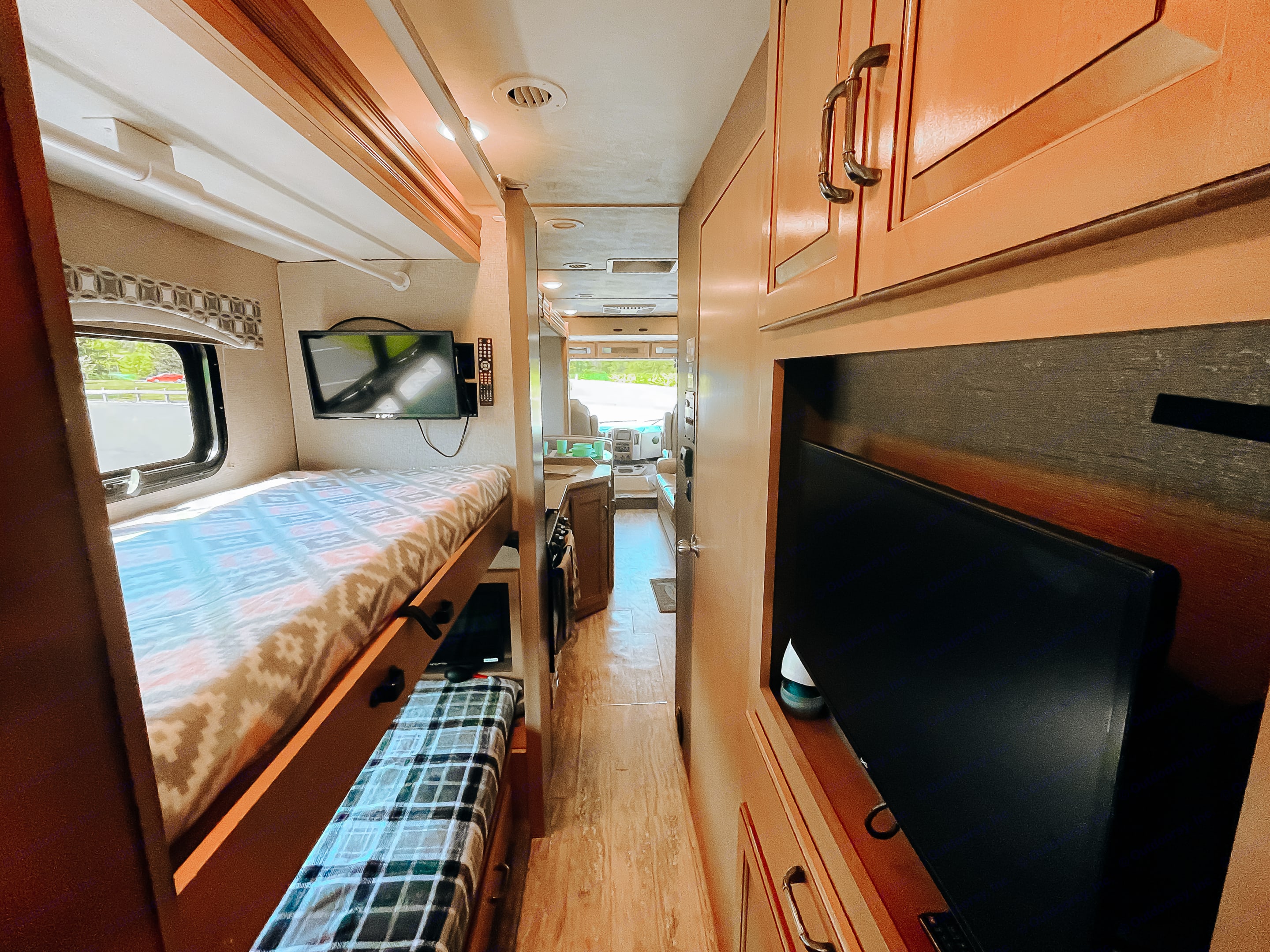 View inside an RV rental, featuring bunk beds on the left, two TVs, and a narrow hallway leading to the front cab.. Thor Hurricane 2017