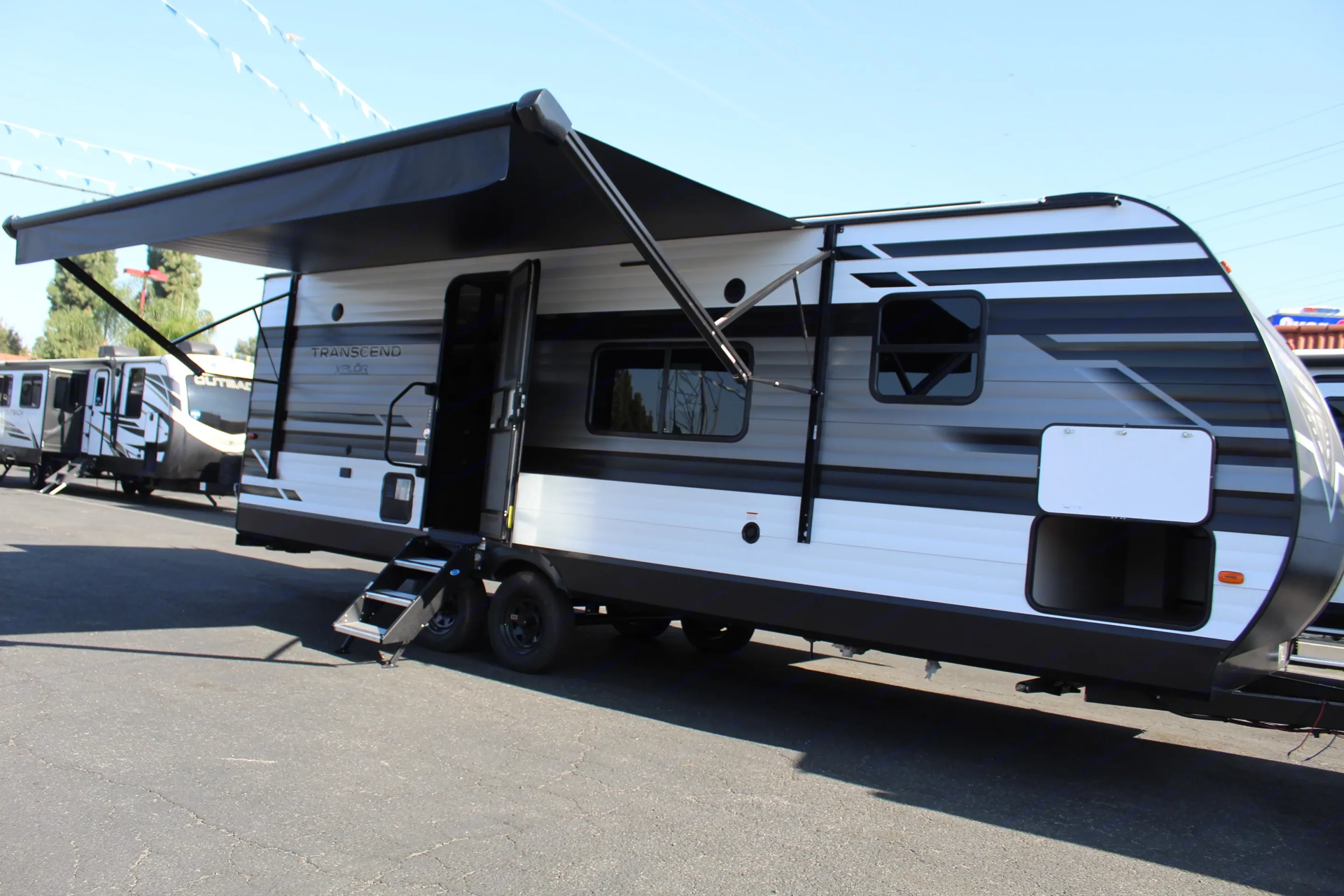 This RV rental, a sleek white and black Transcend XPLOR travel trailer, features an extended awning, open door, and storage.. Grand Design Transcend Xplor 2021