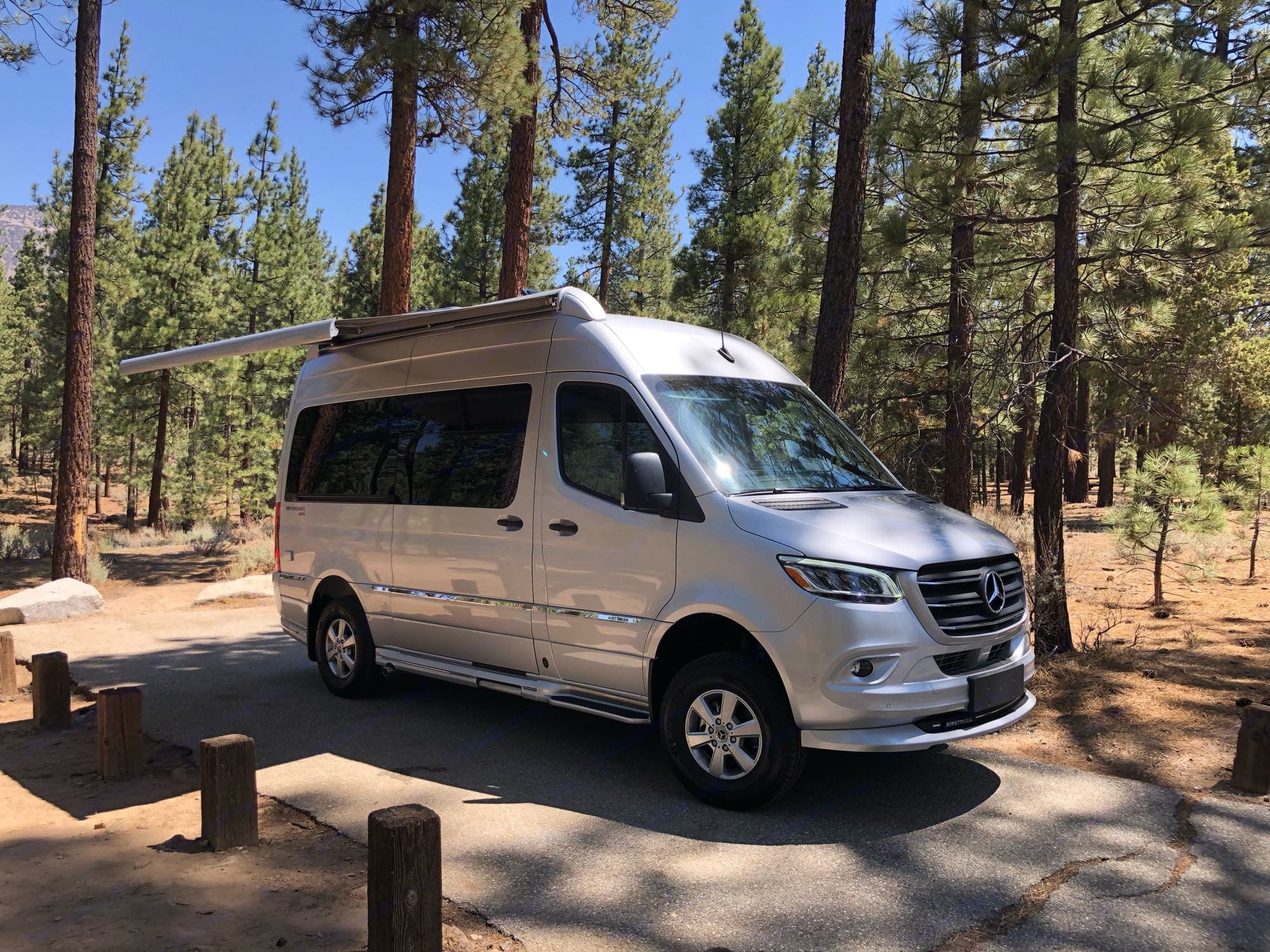 Spacious silver Mercedes-Benz Sprinter van RV rental parked at a serene forest campsite with its awning extended.. Airstream Interstate 2021