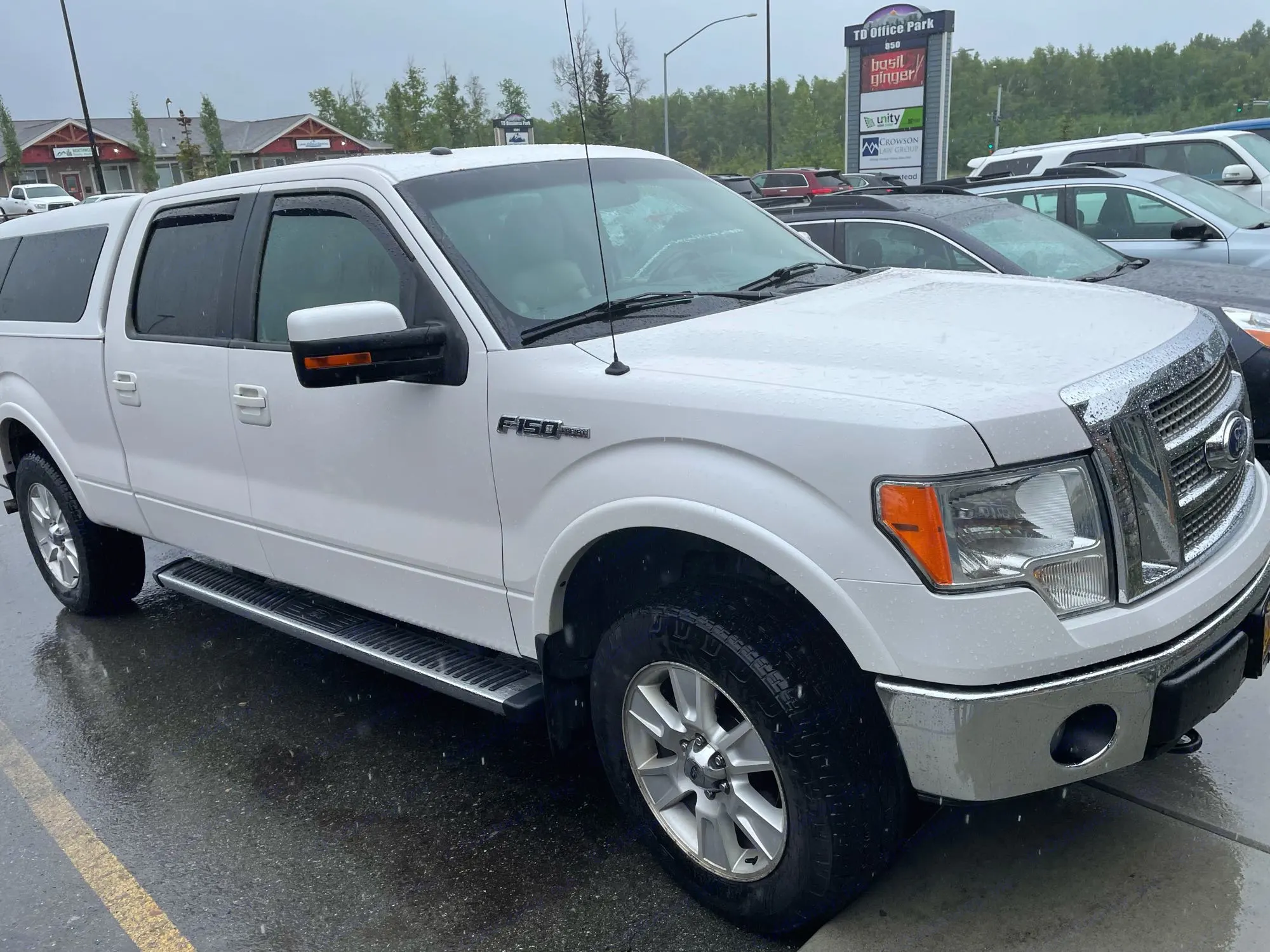 White Ford F-150 pickup truck with a camper shell, wet from rain, parked. Great RV rental alternative for adventures.. Ford Ford F150 2011