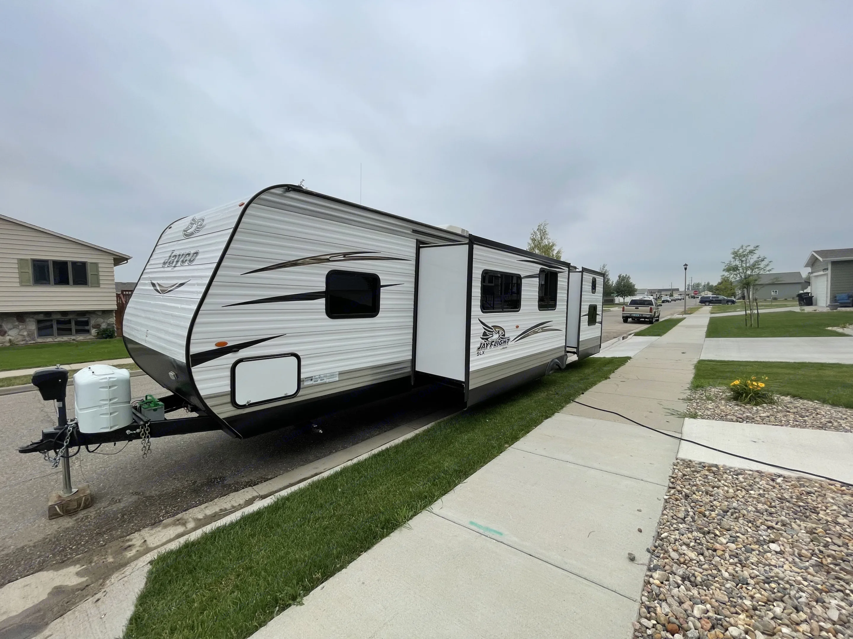 A white Jayco travel trailer, possibly an rv rental, is parked on a residential street with its slide-outs extended.. Jayco Flight SLX 2018