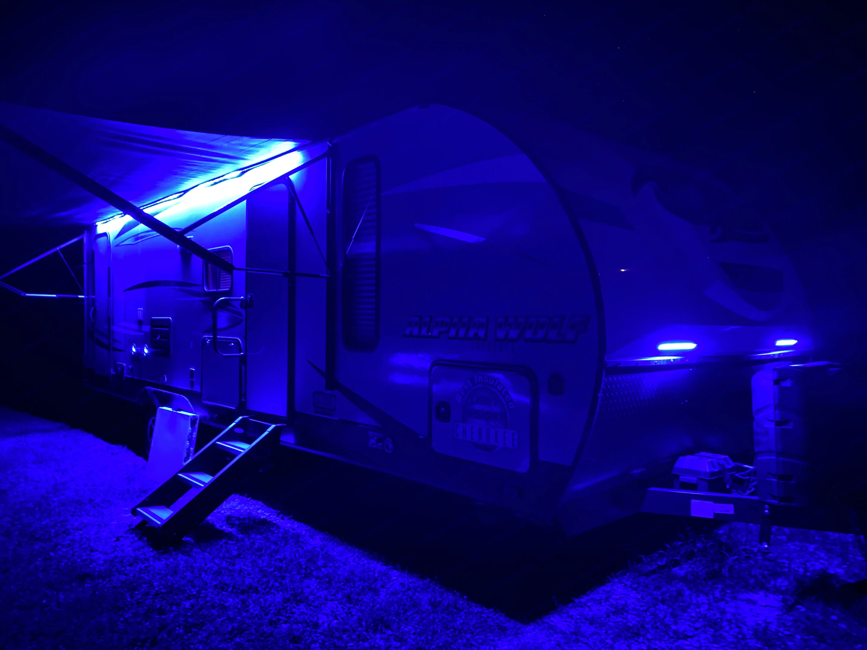 A striking Alpha Wolf travel trailer RV rental at night, illuminated by vibrant blue LED lights under its awning and on the front.. Forest River Alpha Wolf 2020