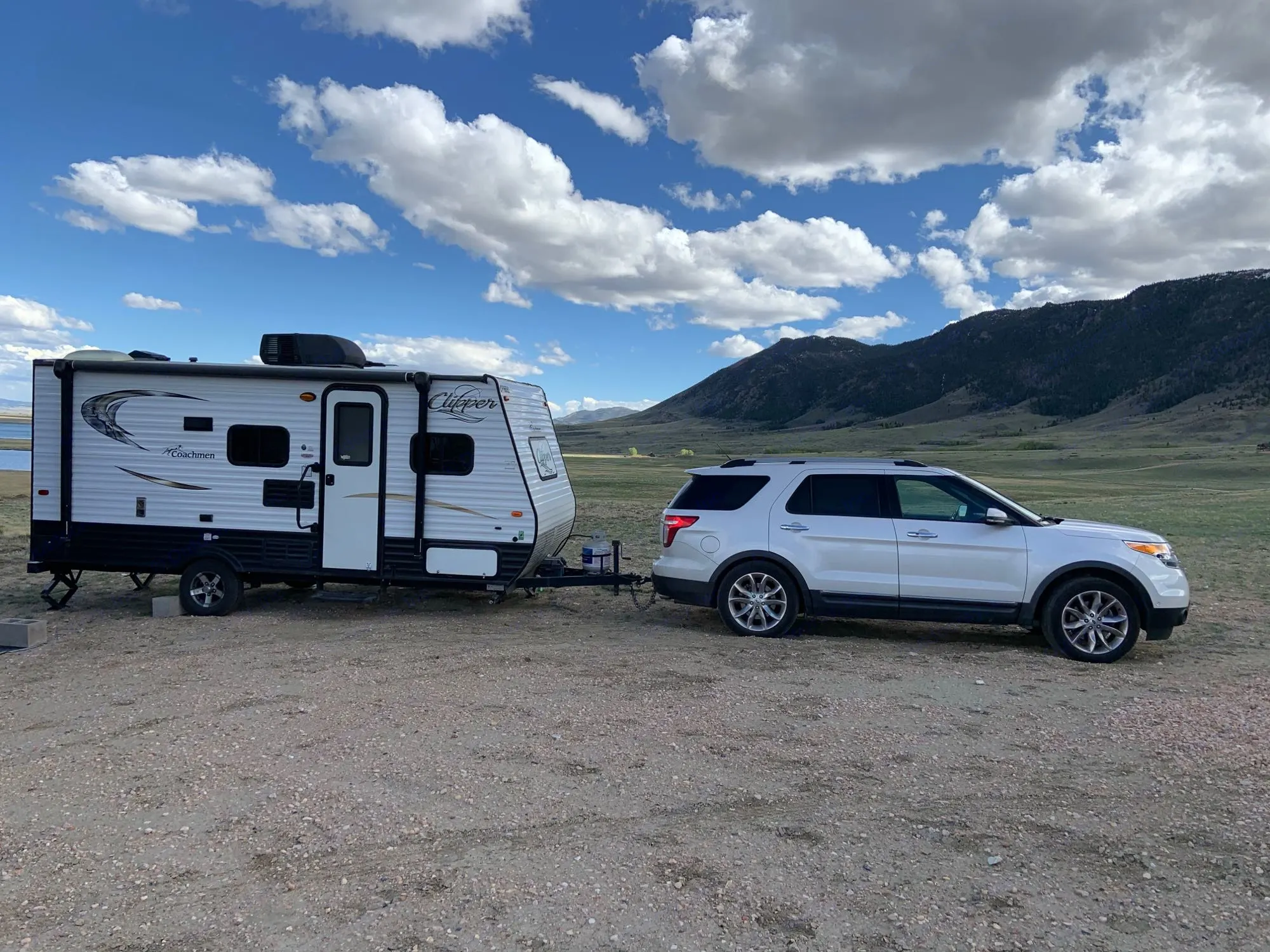 White RV rental & SUV parked by a lake and mountains, perfect for camping. Enjoy nature's beauty on your next adventure.. Coachmen Clipper 2015