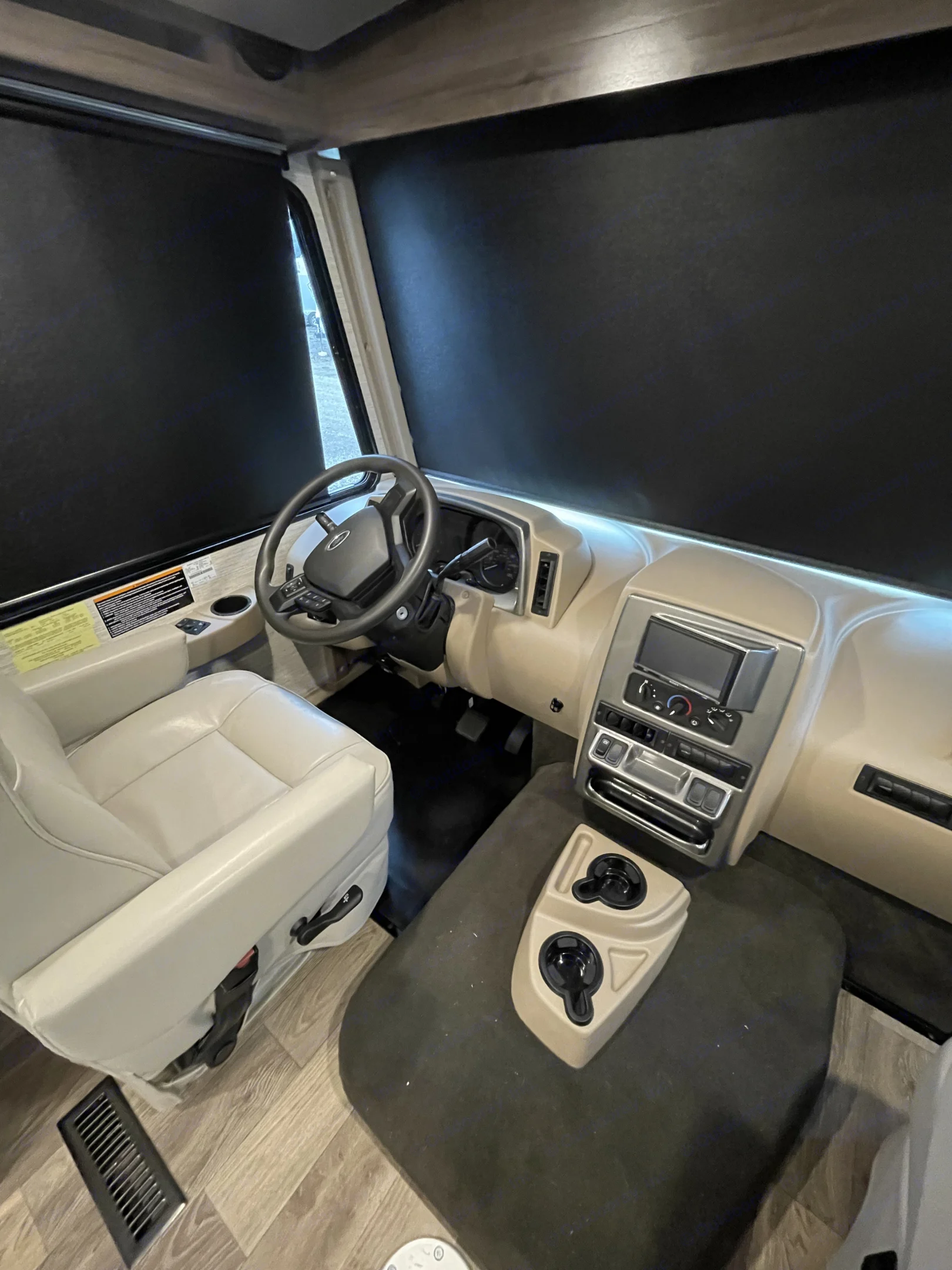 Explore this RV rental's spacious cockpit. Features a beige dashboard, steering wheel, driver's seat, and black privacy shades.. Winnebago Vista 2022