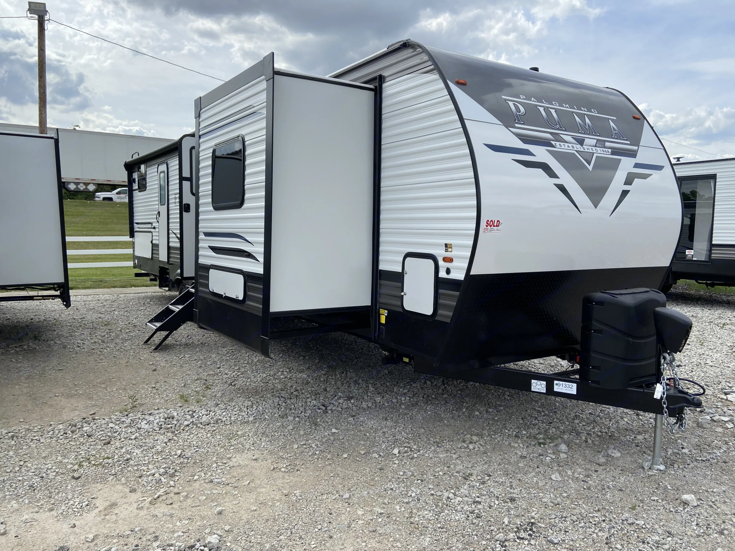 A white & black Palomino Puma travel trailer RV with extended slide-out on a gravel lot. Great for an rv rental.. Forest River Puma 2021