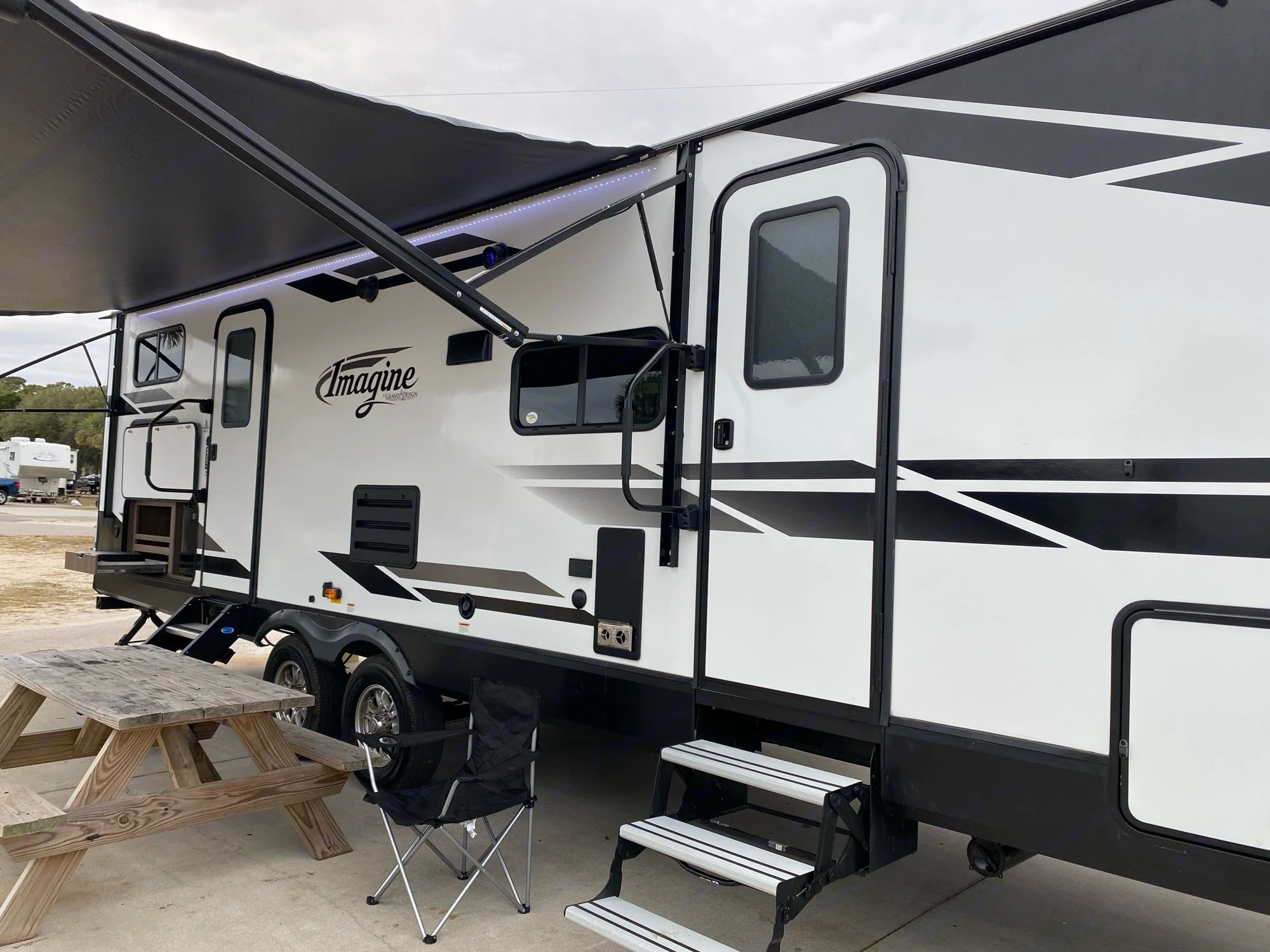 This white & black travel trailer RV rental is parked at a campsite with an open awning, picnic table, and chair.. Grand Design Imagine 2800BH #1 2021