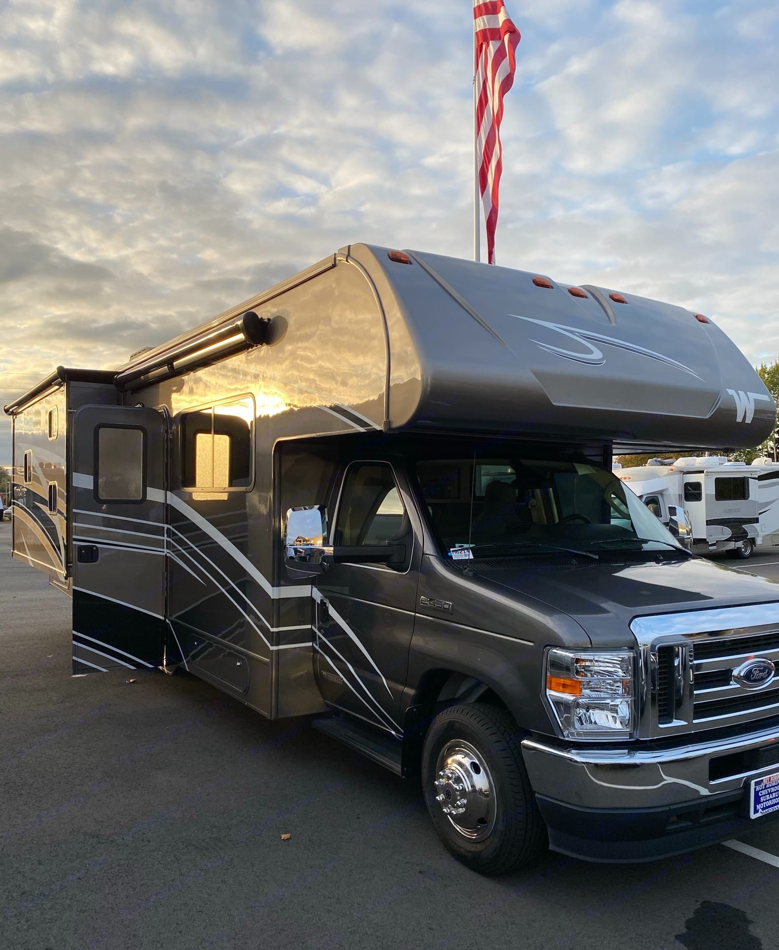 Experience freedom with this Class C RV rental. A large dark grey motorhome with an extended slide-out, parked under a cloudy sky.. Winnebago Minnie Winnie 2021