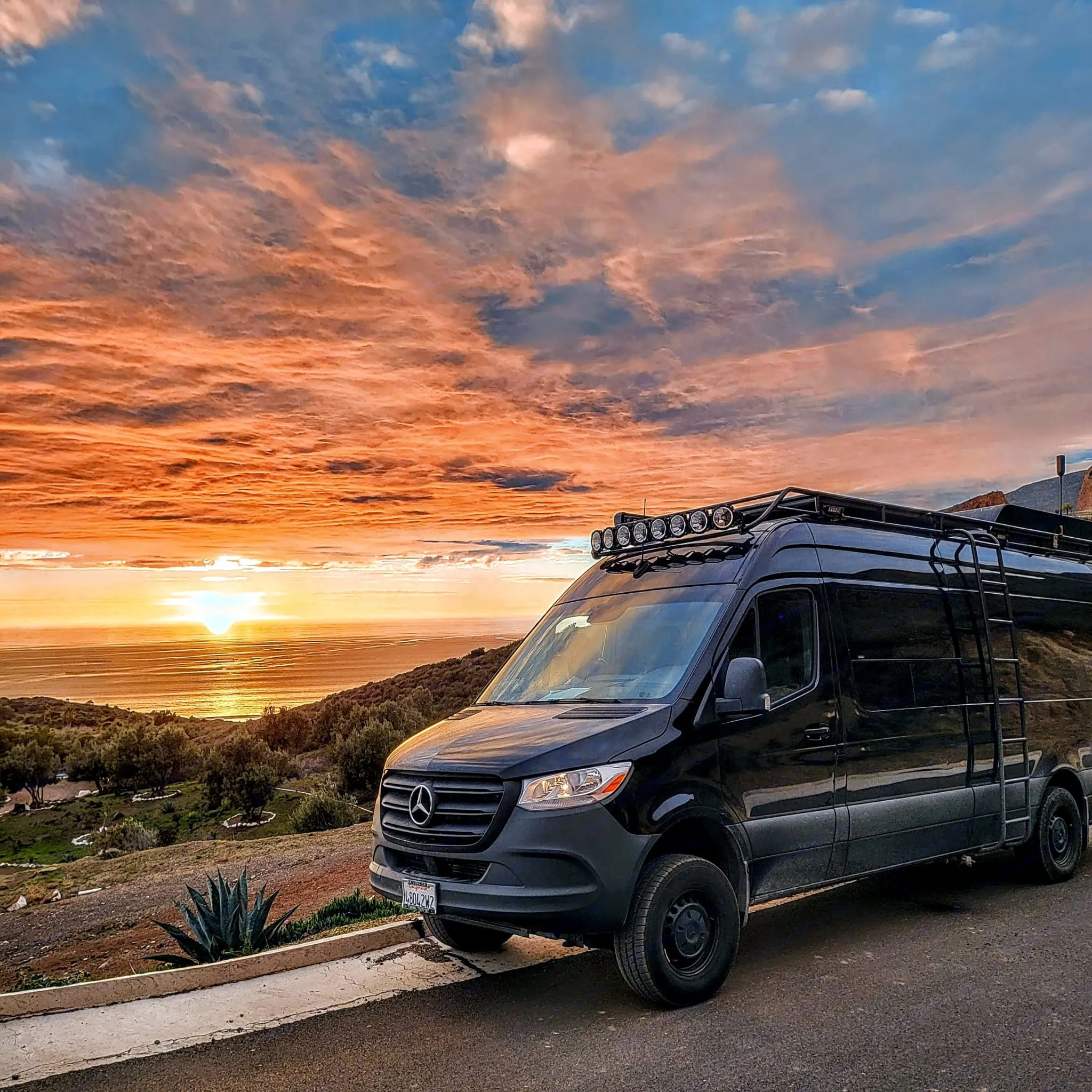 Black Mercedes camper van parked at a scenic ocean overlook during a vivid sunset. Consider this rv rental for your next trip!. Mercedes-Benz Sprinter 2019