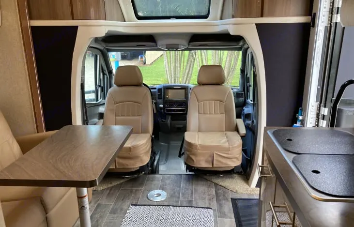RV rental interior showcases driver's cockpit, swiveling front seats, and a compact living area with din. Winnebago View 2018
