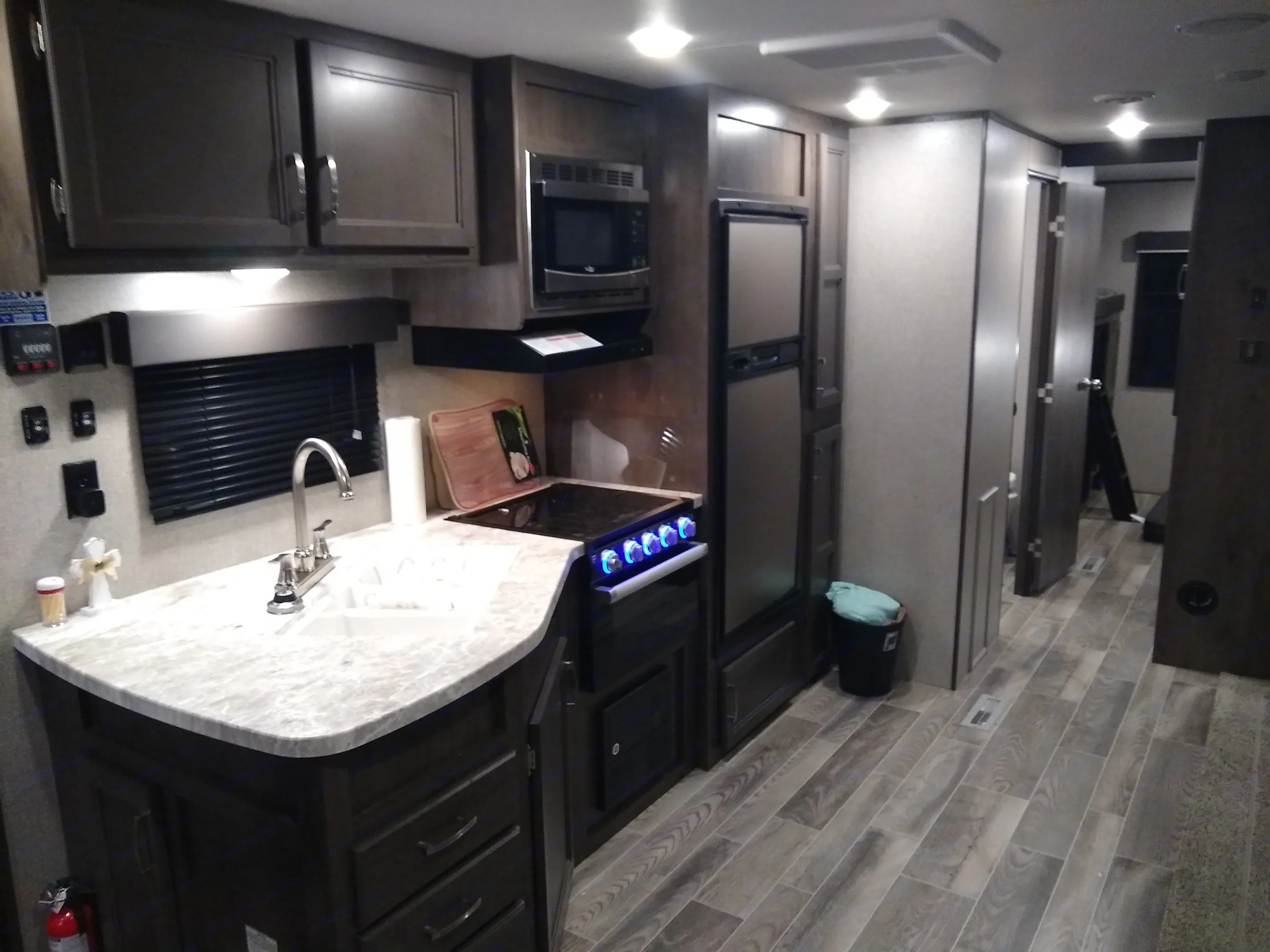 Inside a modern RV rental: A kitchen with dark cabinets, light counters, sink, stove, microwave, fridge, and wood-look floors.. Jayco Jay Flight SLX 2021