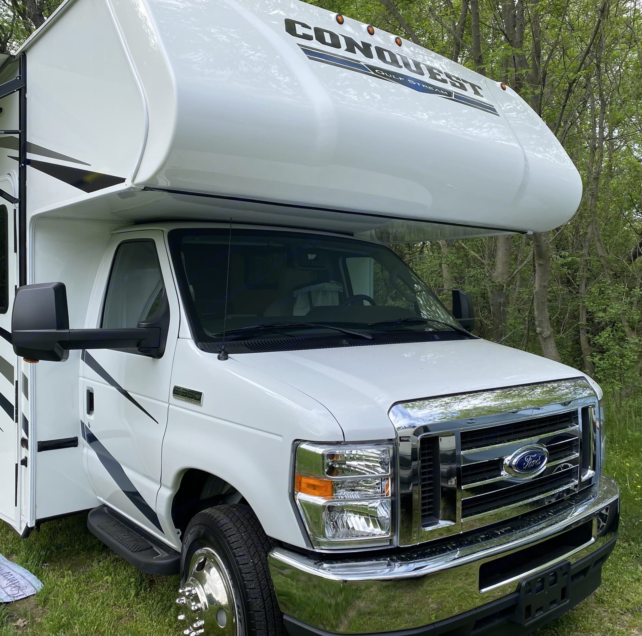 White Conquest Gulf Stream Class C RV rental, built on a Ford E-350 chassis, parked on grass with trees.. Gulf Stream Conquest 2022