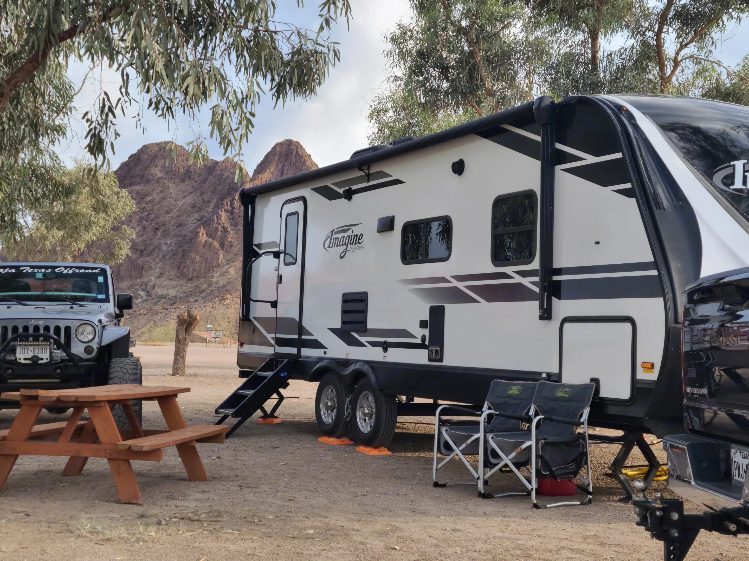 Scenic desert rv rental campsite with a Grand Design Imagine RV, Jeep, truck, and picnic table amidst mountains.. Grand Design Imagine 2021