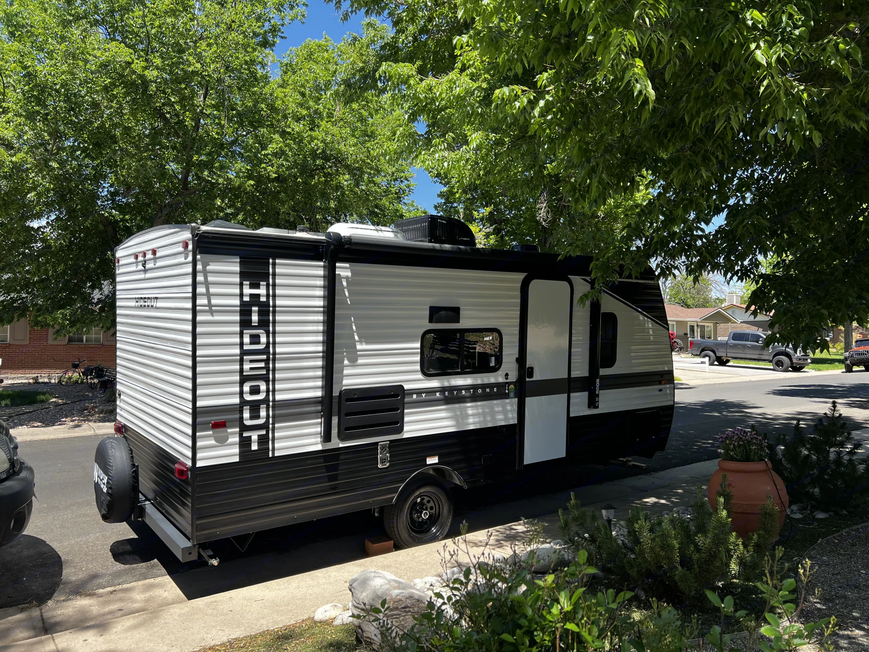 White and black Hideout travel trailer, great for an RV rental adventure, parked on a sunny residential driveway under a tree.. Keystone Hideout 2022