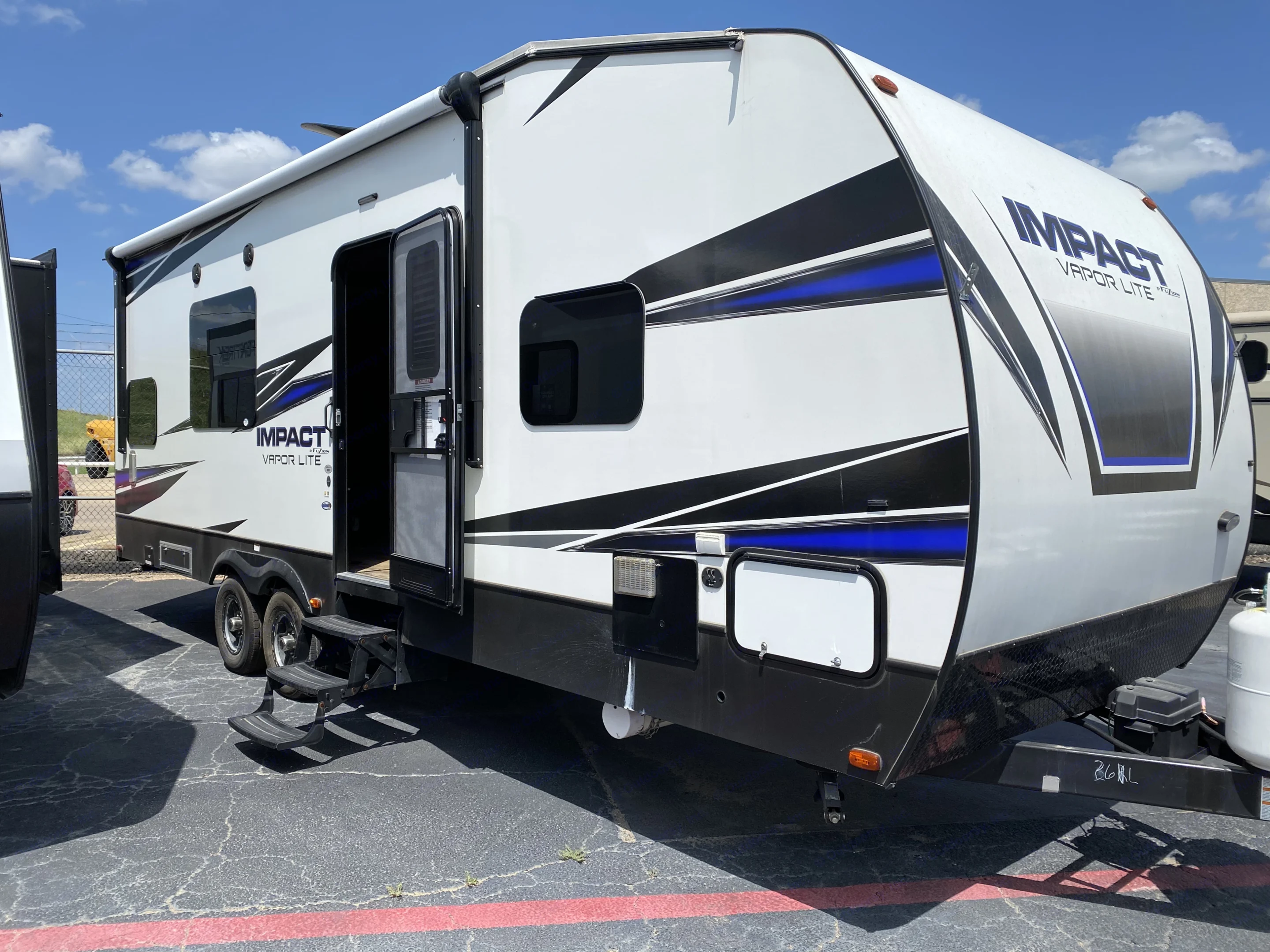 A white and black Impact Vapor Lite travel trailer, with blue accents, parked outdoors with its door open, available for RV rental.. Keystone Impact 2019