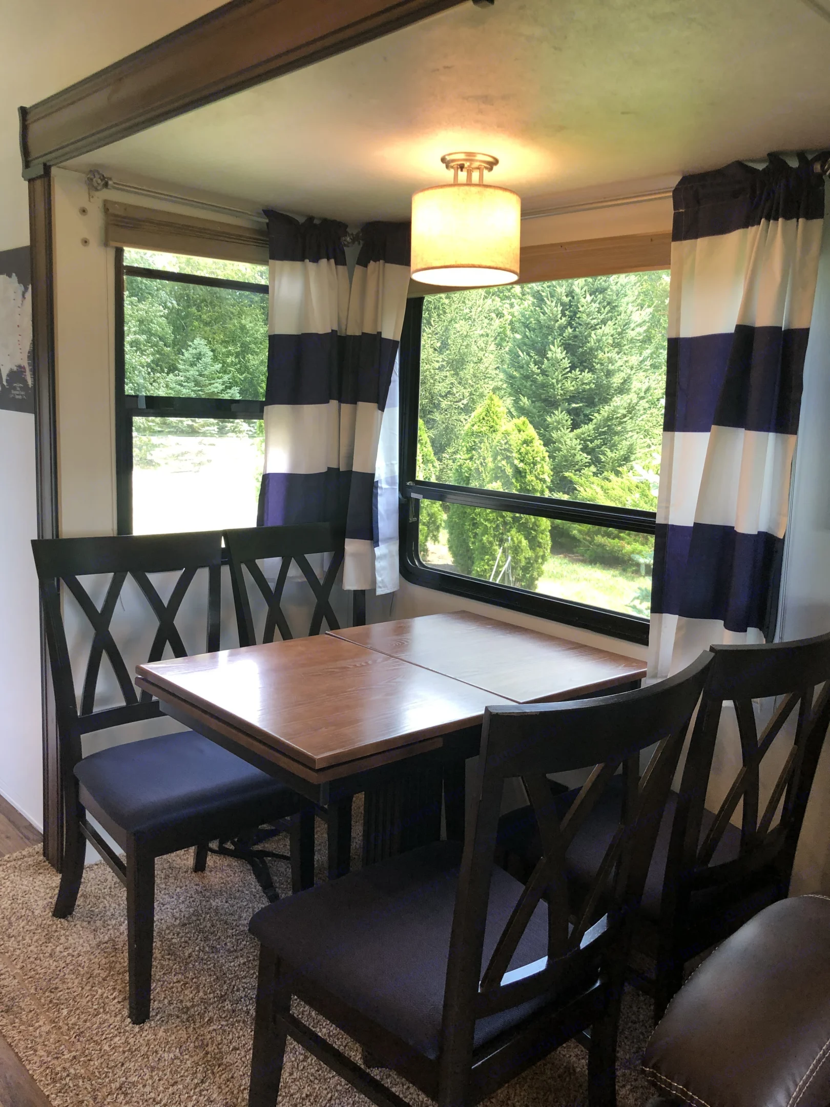 RV rental interior: cozy dining area featuring a wooden table, dark chairs, striped curtains, and a lush green window view.. Forest River Coachmen Chaparral 2018