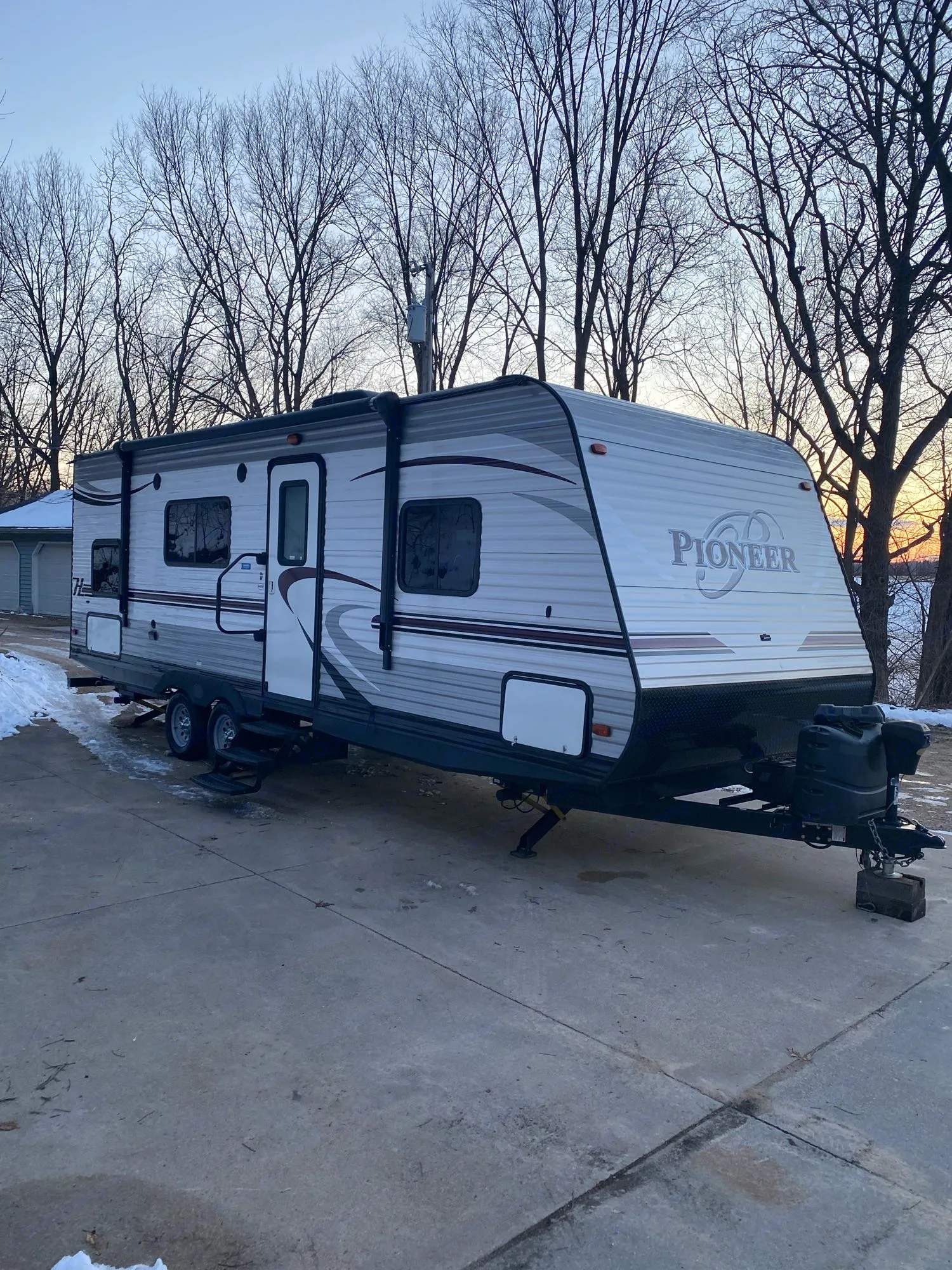 Pioneer travel trailer, ideal for an RV rental, parked on a snowy driveway with bare trees and a beautiful sunset.. Heartland RVs Pioneer 2016