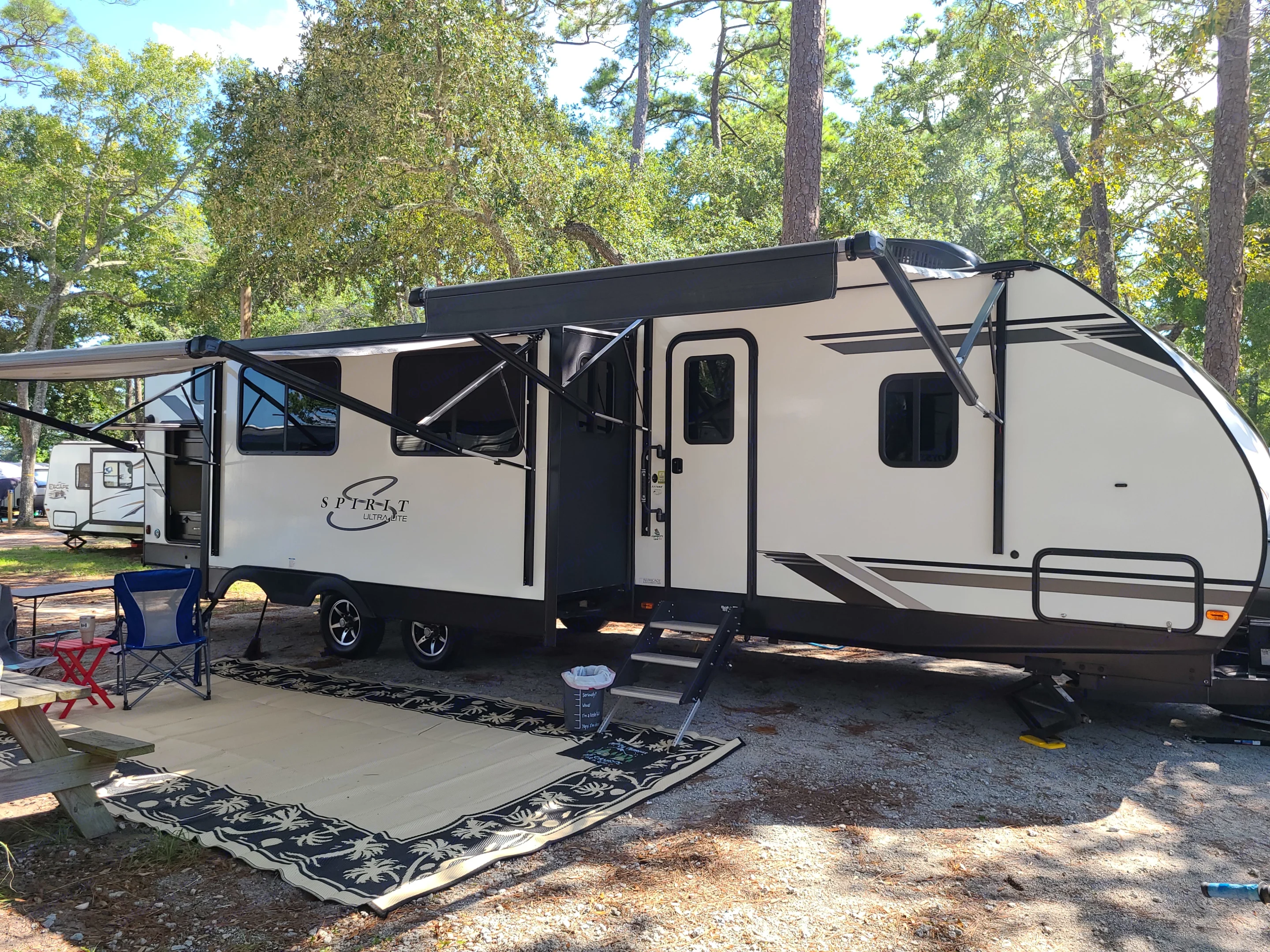 Entrance side with two awnings and dining area slide. Area rug and camp chairs. Coachmen Spirit Ultralight 2020