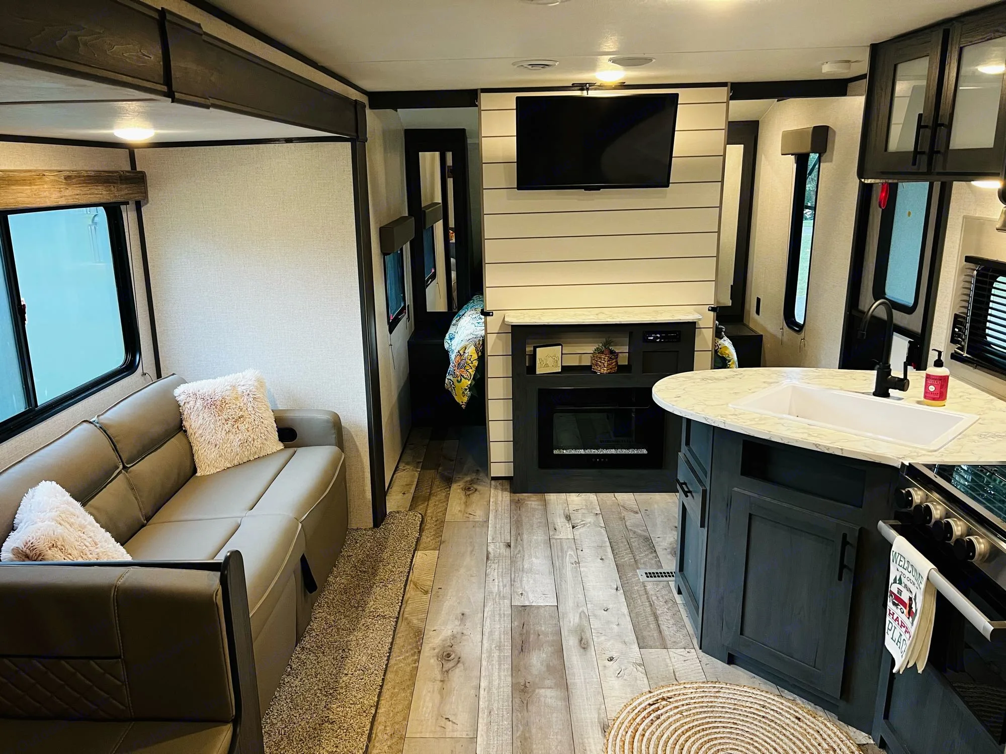 Cozy modern RV interior featuring a living area with a sofa, TV, and fireplace, plus a kitchen with a sink. Great for. Dutchmen Aspen Trail LE 2023