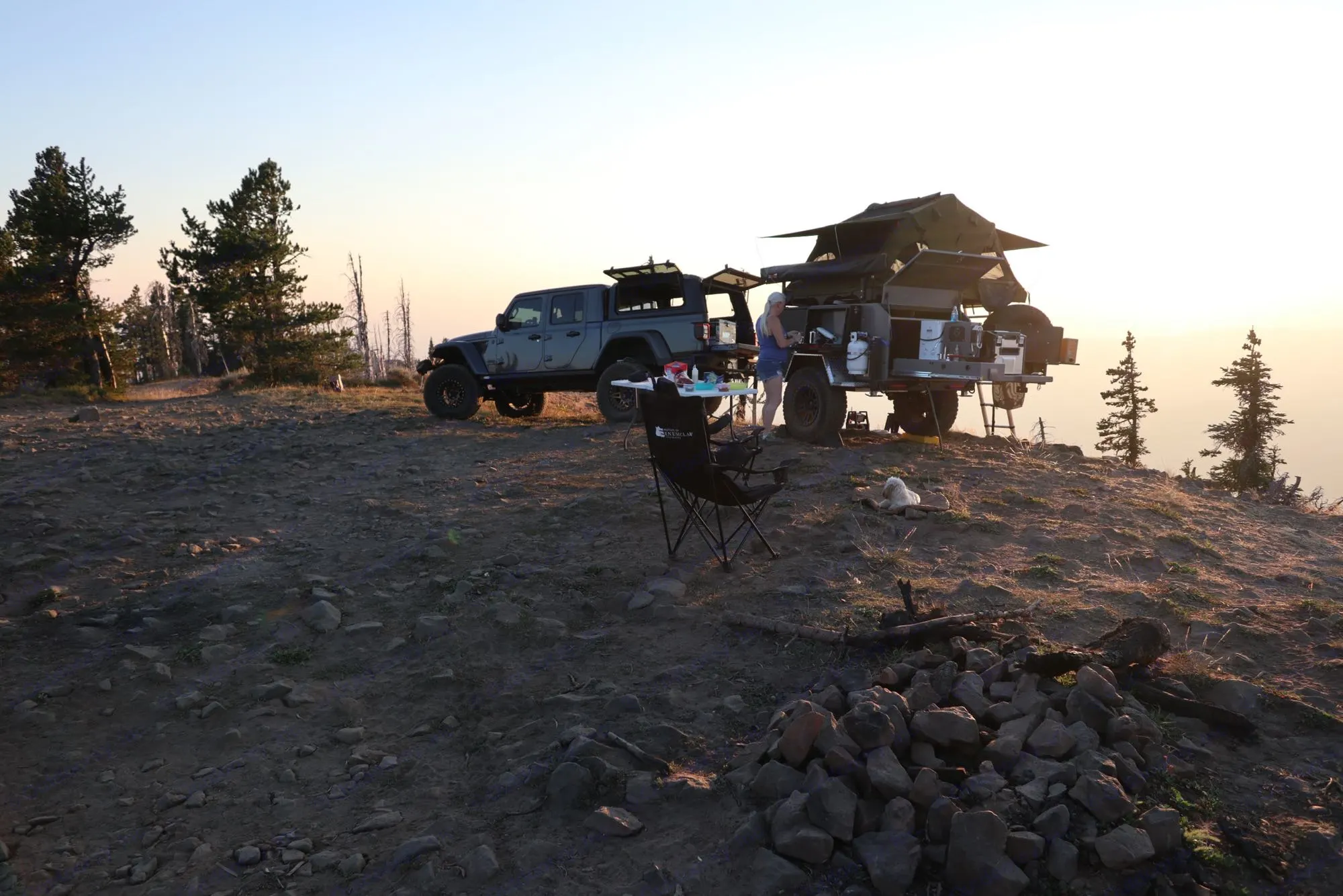 Scenic overlanding camp: Jeep & trailer with rooftop tent, person, dog, & fire pit at sunset. A rugged RV rental experience.. Vorsheer XER 2022