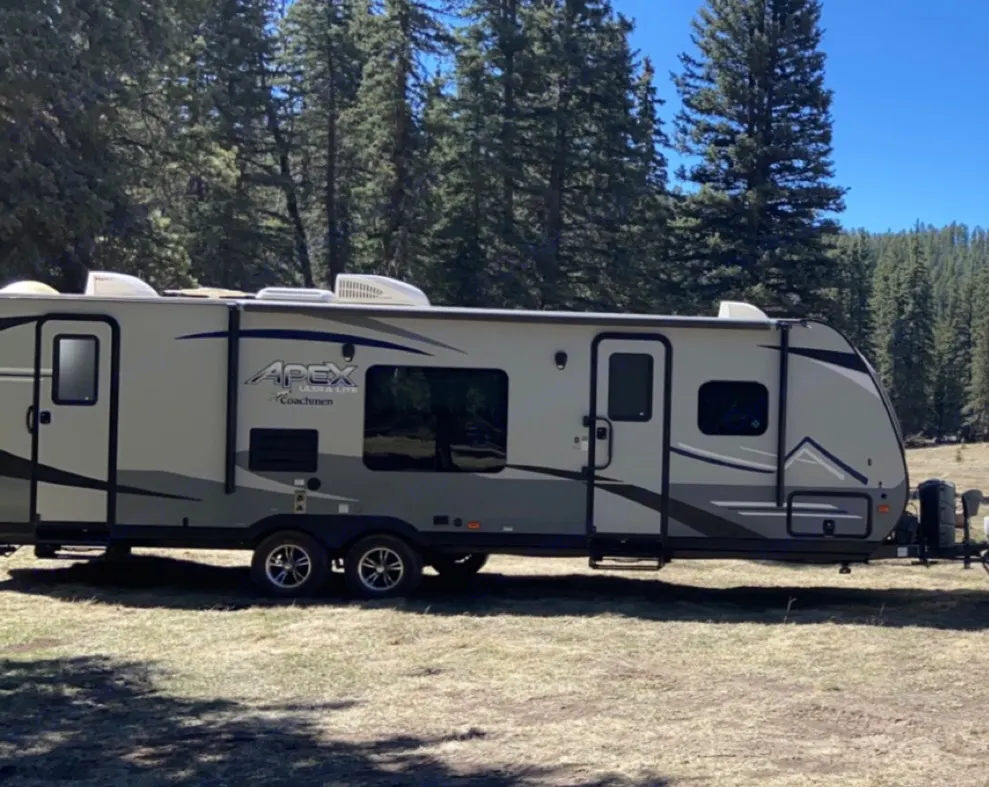 This sleek Apex Ultra Lite RV rental is parked in a sunny, forested campground, ideal for outdoor adventures.. Coachmen Apex 2019