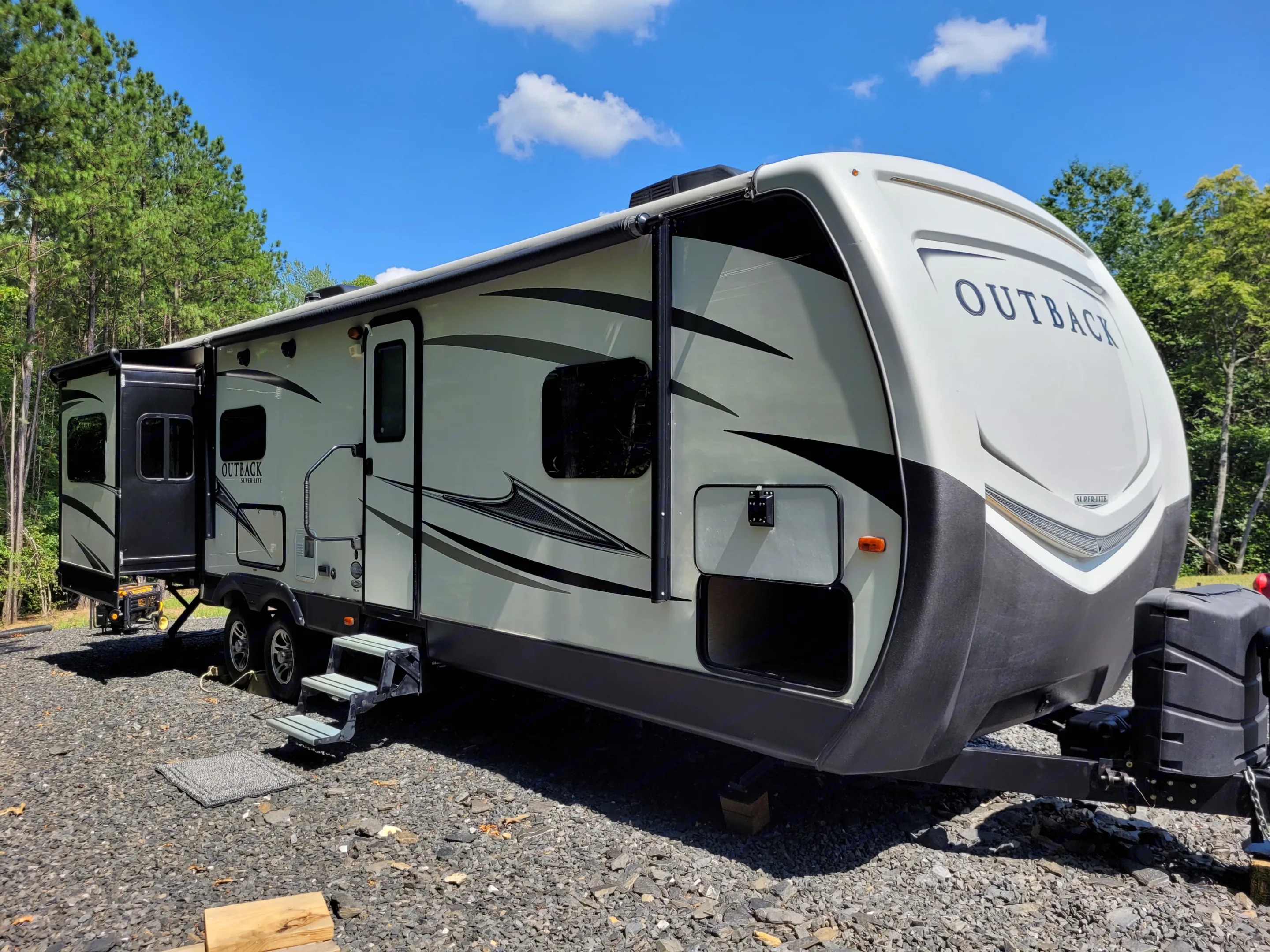Bright Outback travel trailer RV rental, slide-out extended, parked on gravel in a wooded, sunny setting.. Keystone RV Outback Super-Lite 2017