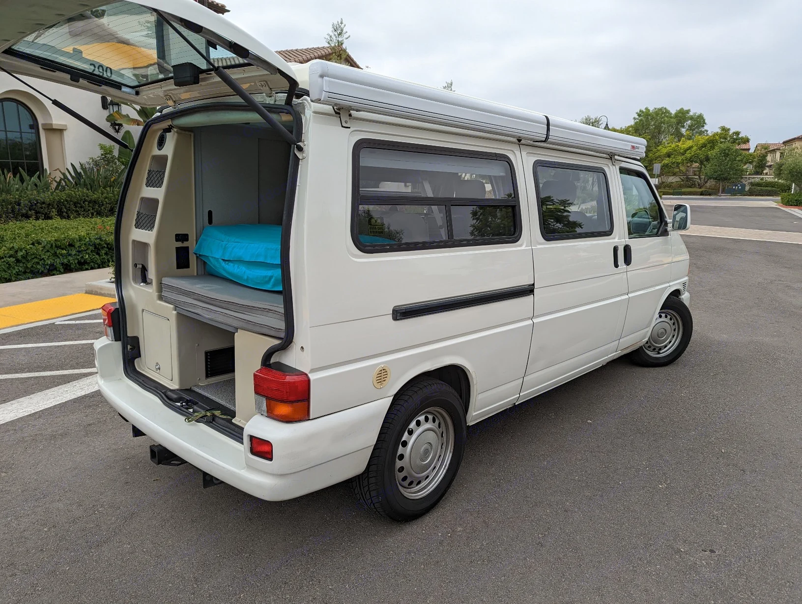 White camper van, perfect for RV rental adventures, with open rear hatch showing sleeping setup.. Volkswagen Eurovan 2001