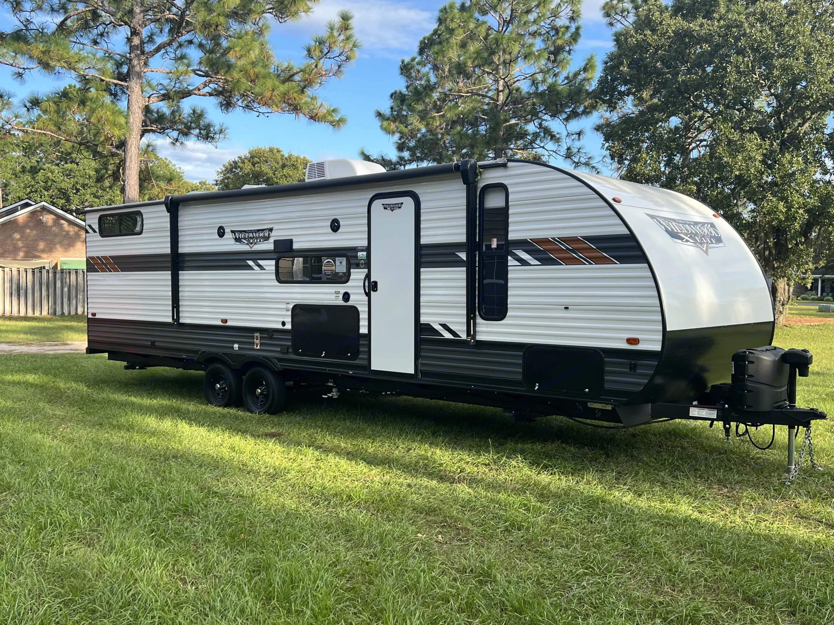 A white Wildwood X-Lite travel trailer, ideal for an RV rental, is parked on bright green grass outdoors.. Forest River Wildwood X-Lite 2022
