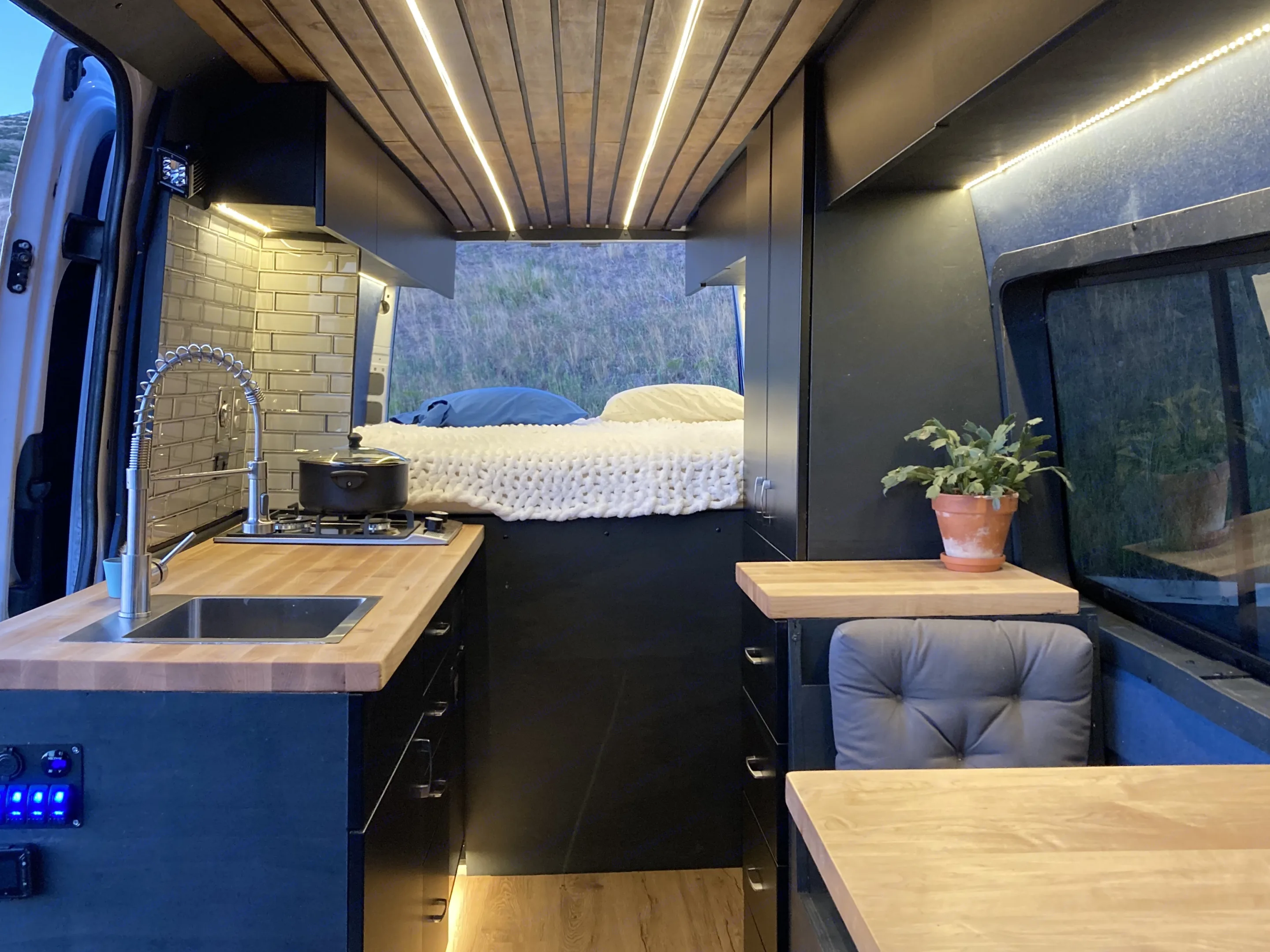 Inside a well-designed RV rental: compact kitchen with sink/stove, cozy rear bed, dining area, and sleek dark cabinetry.. Mercedes Sprinter 2015