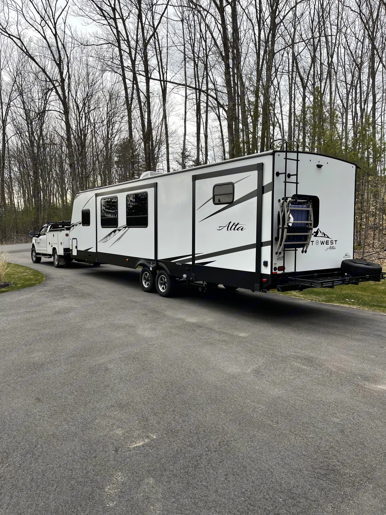 White pickup truck towing a spacious Alta travel trailer RV on an asphalt driveway. Perfect rv rental for your next trip.. East to West Alta 2022