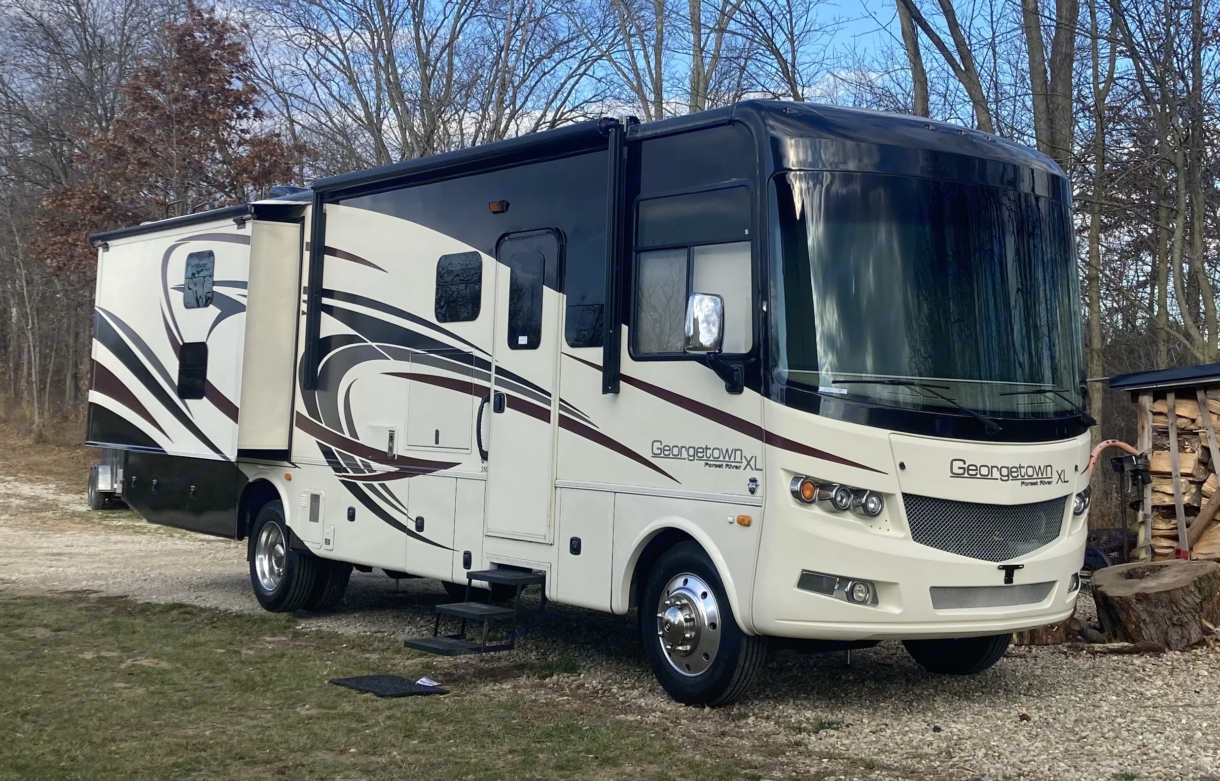 A large white and black Georgetown XL rv rental motorhome with slide-outs extended, parked on a gravel drive with trees.. Georgetown XL 2015