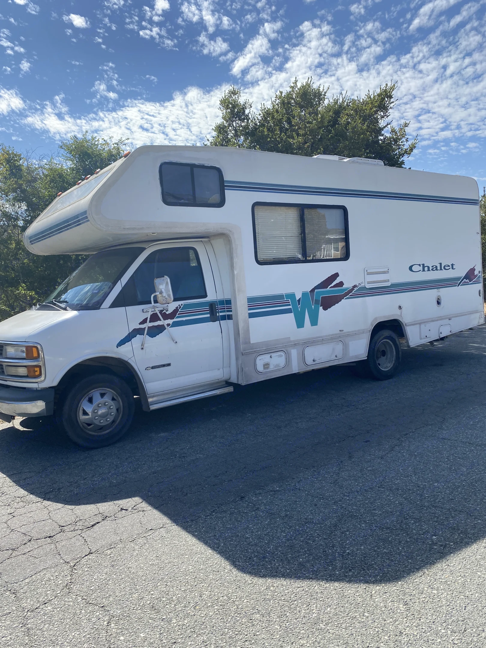 White Chalet RV rental with blue & brown graphics, parked on cracked asphalt under a bright sky with white clouds.. Winnebago Chalet 2000