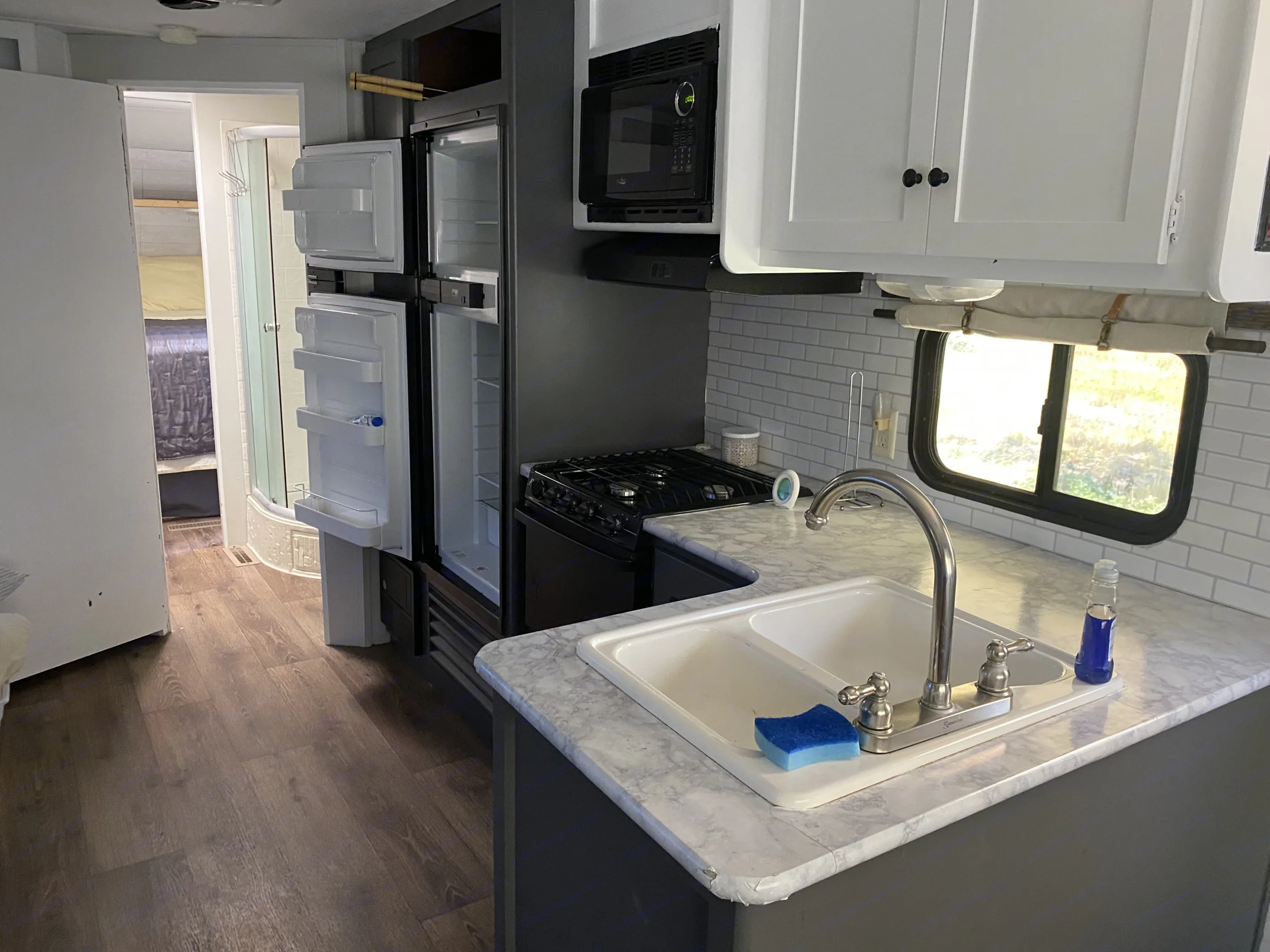 Inside an RV rental: a bright, updated kitchen featuring a sink, stove, fridge, microwave, and subway tile backsplash. Aspen Trail Aspen Trail Trailer 2015