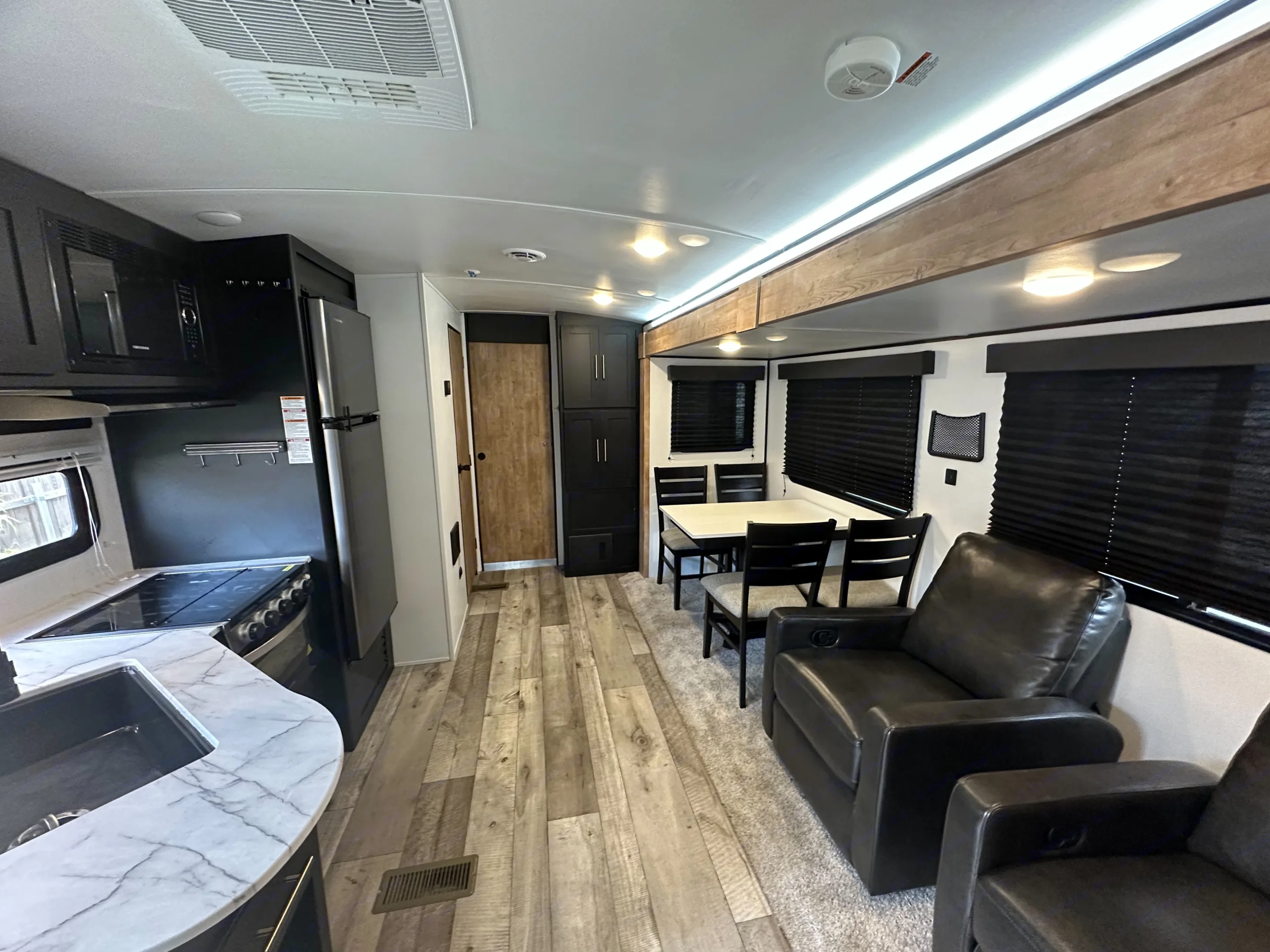 Inside this modern rv rental: full kitchen, dining table, and plush seating. Light-colored flooring and dark cabinets.. Keystone RV Springdale 2022