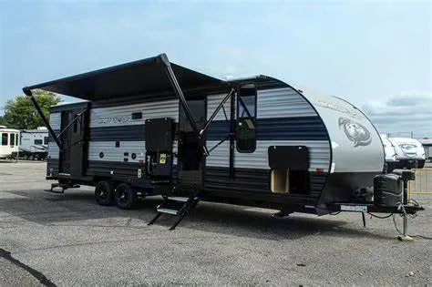 This blue and grey travel trailer with an extended awning is parked and ready for an RV rental adventure.. Forest River Cherokee Grey Wolf 2021