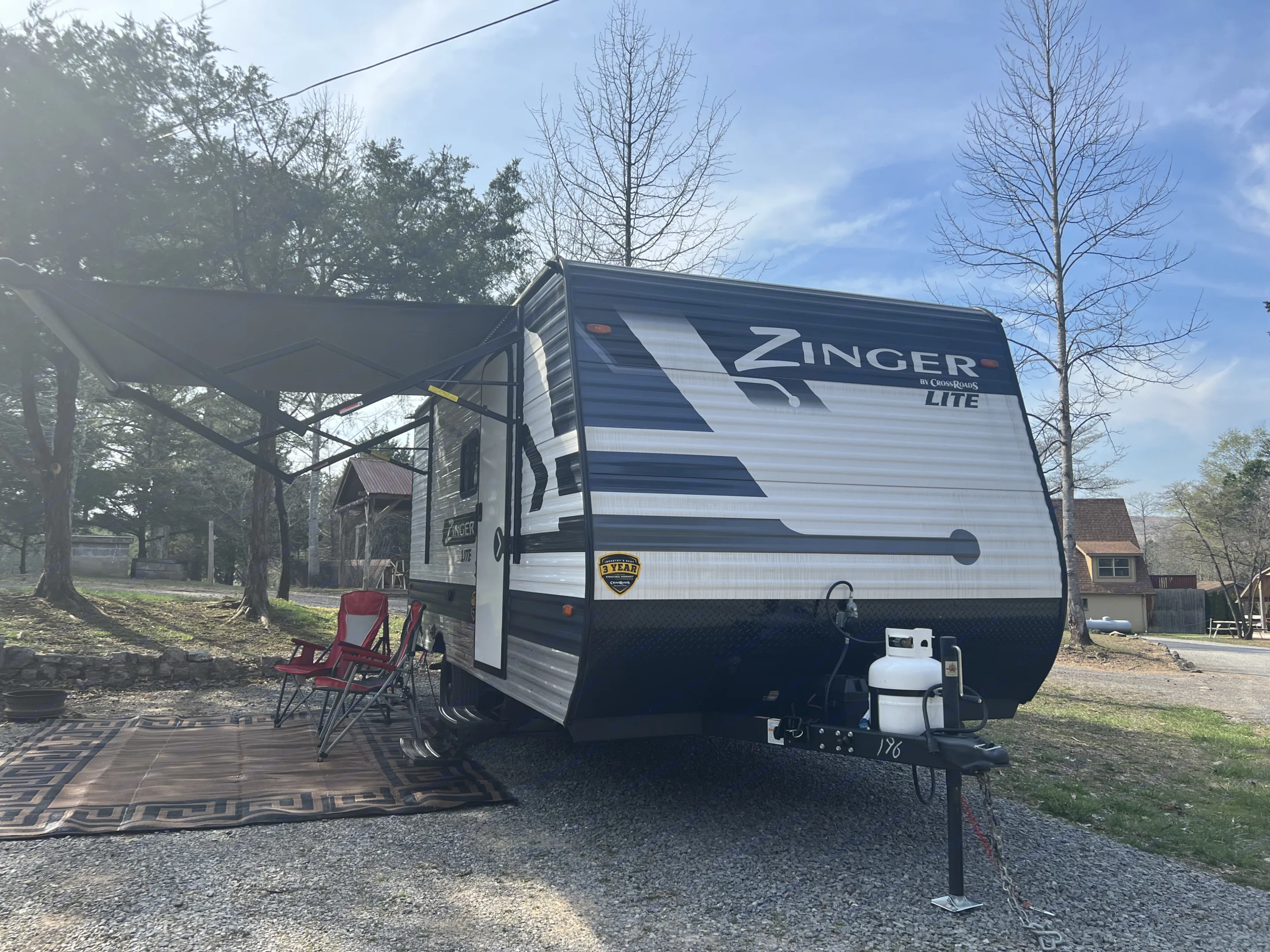 Enjoy your RV rental! This Zinger Lite travel trailer is set up with an extended awning, chairs, and mat at a sunny campsite.. Crossroads Zinger Lite 2022