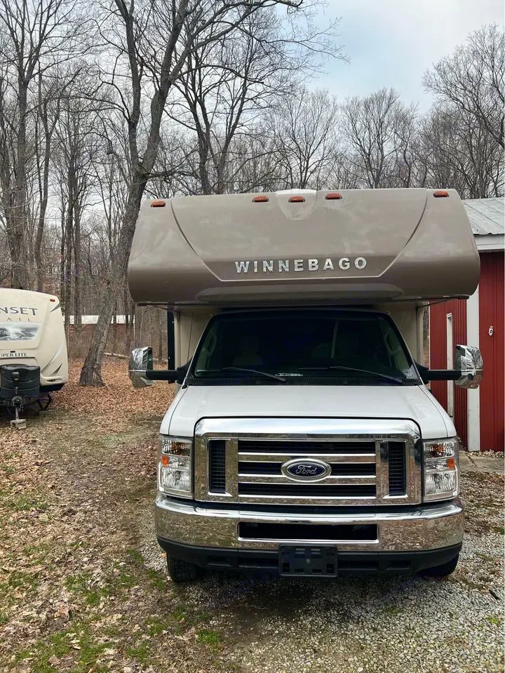 Front view of a white Winnebago Class C RV for RV rental, parked outdoors among bare trees, ready for travel & camping.. Winnebago Minnie Winnie 2017