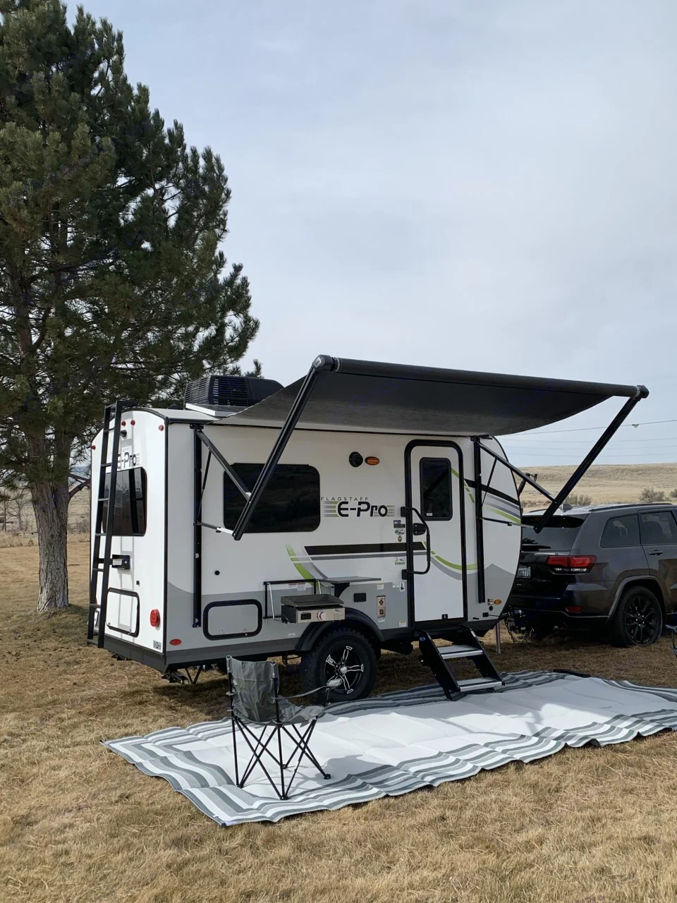 An E-Pro RV rental with its awning extended, featuring an outdoor mat and chair on dry grass. Ready for camping.. Forest River Flagstaff E-Pro 2022