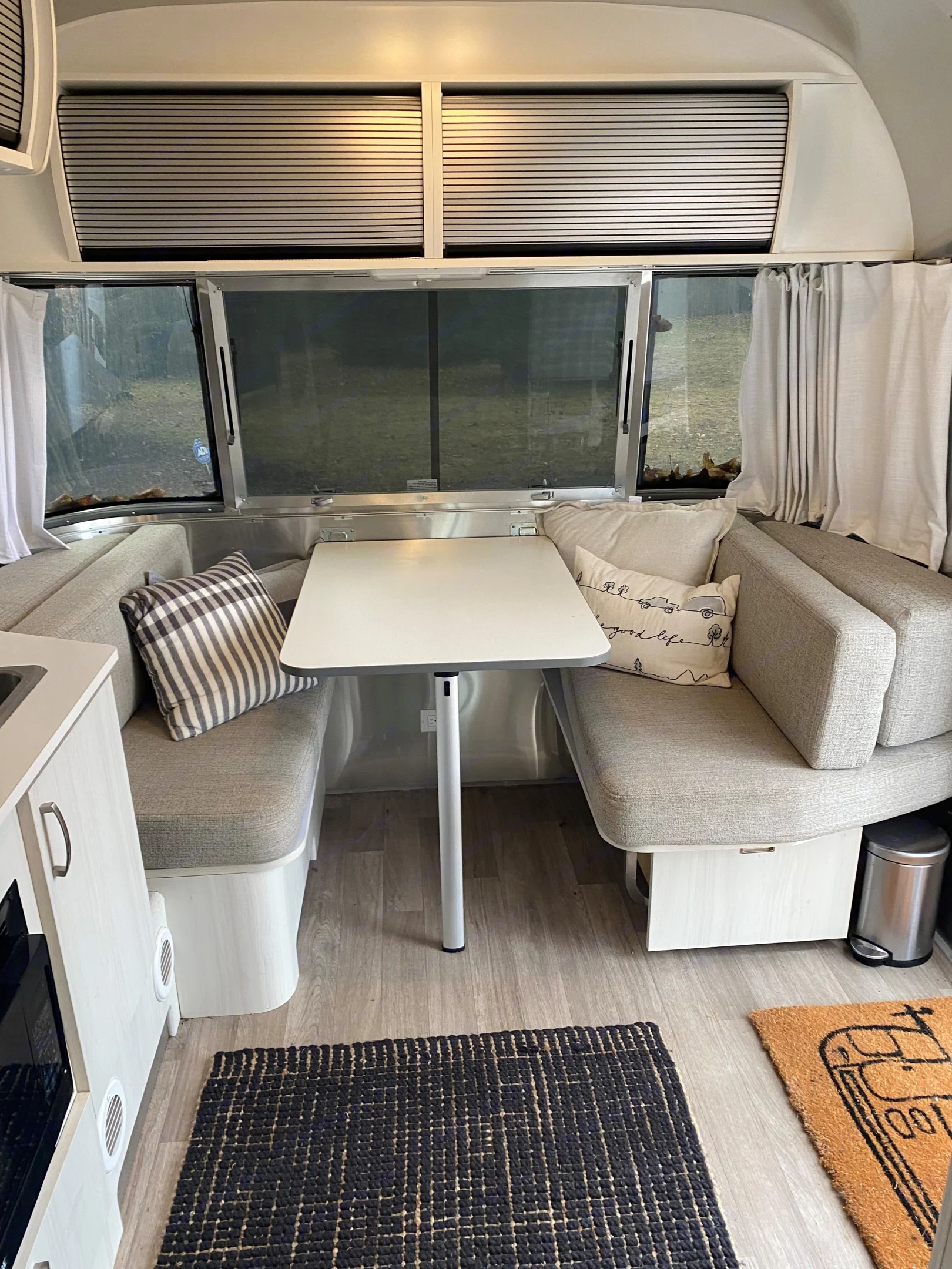 This RV rental boasts a bright, inviting dinette area with grey upholstered benches, a central table, and scenic windows.. Airstream Bambi 2022