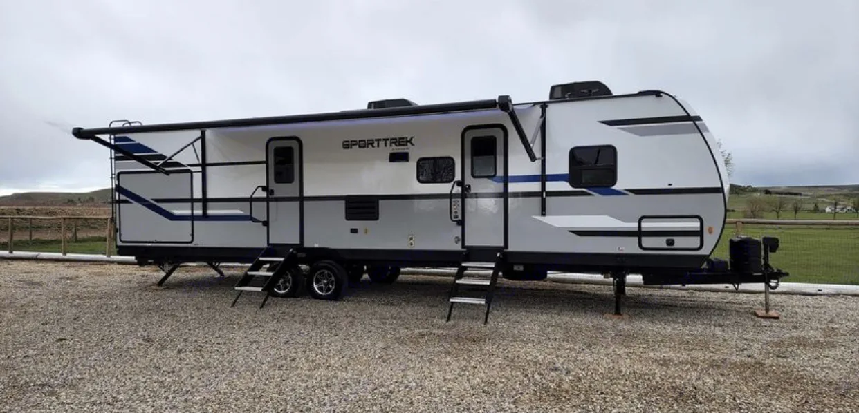 Spacious white & grey RV rental with extended awning parked on gravel. Perfect for travel and camping adventures.. Venture Sporttrek 2022