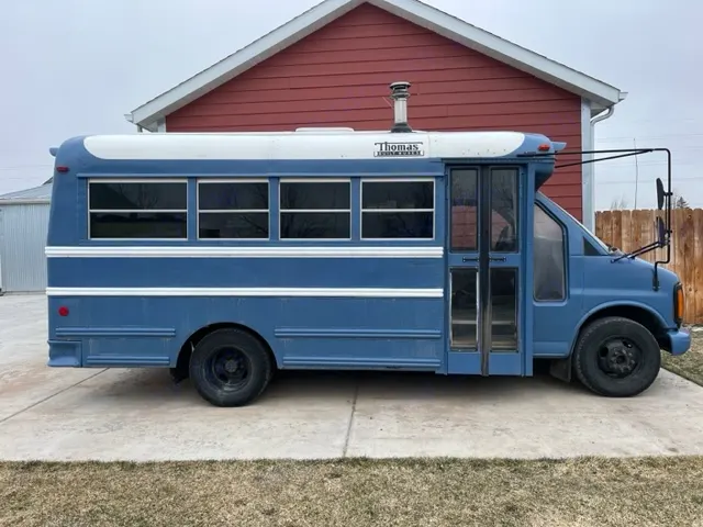 Blue Thomas school bus converted to RV, featuring a chimney & tinted windows, perfect for an rv rental.. GMC Savana 2002