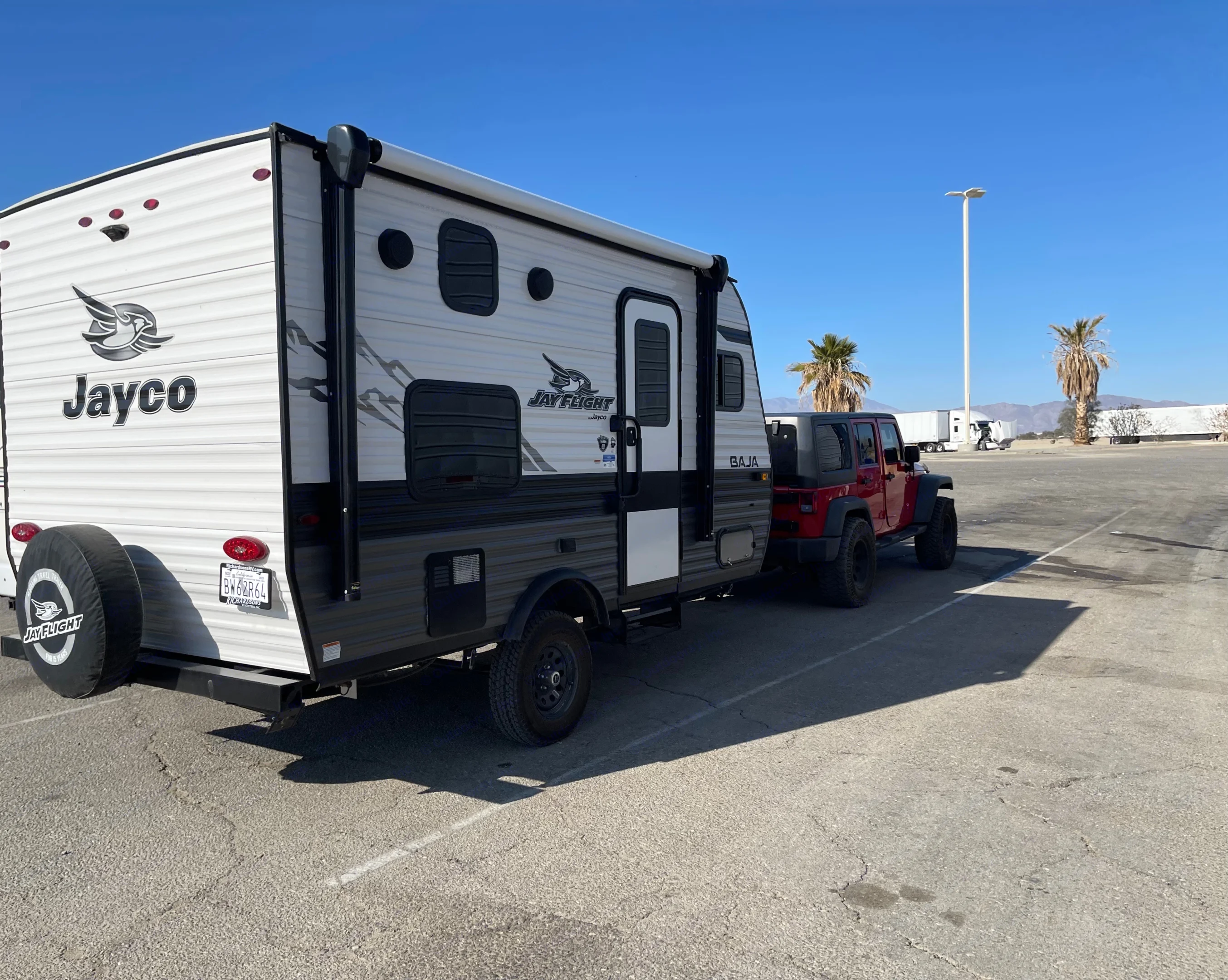 Red Jeep towing a Jayco Jay Flight Baja RV rental travel trailer, parked for a sunny road trip. Perfect for outdoor camping adventures!. Jayco Jay Flight SLX Baja Edition 2022