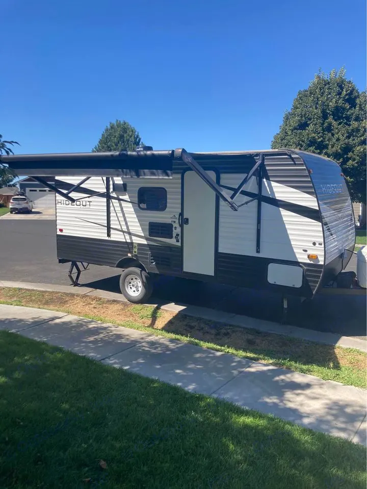 A white and black Hideout travel trailer is parked with its awning extended, ready for your next RV rental.. Keystone RV Hideout 2022