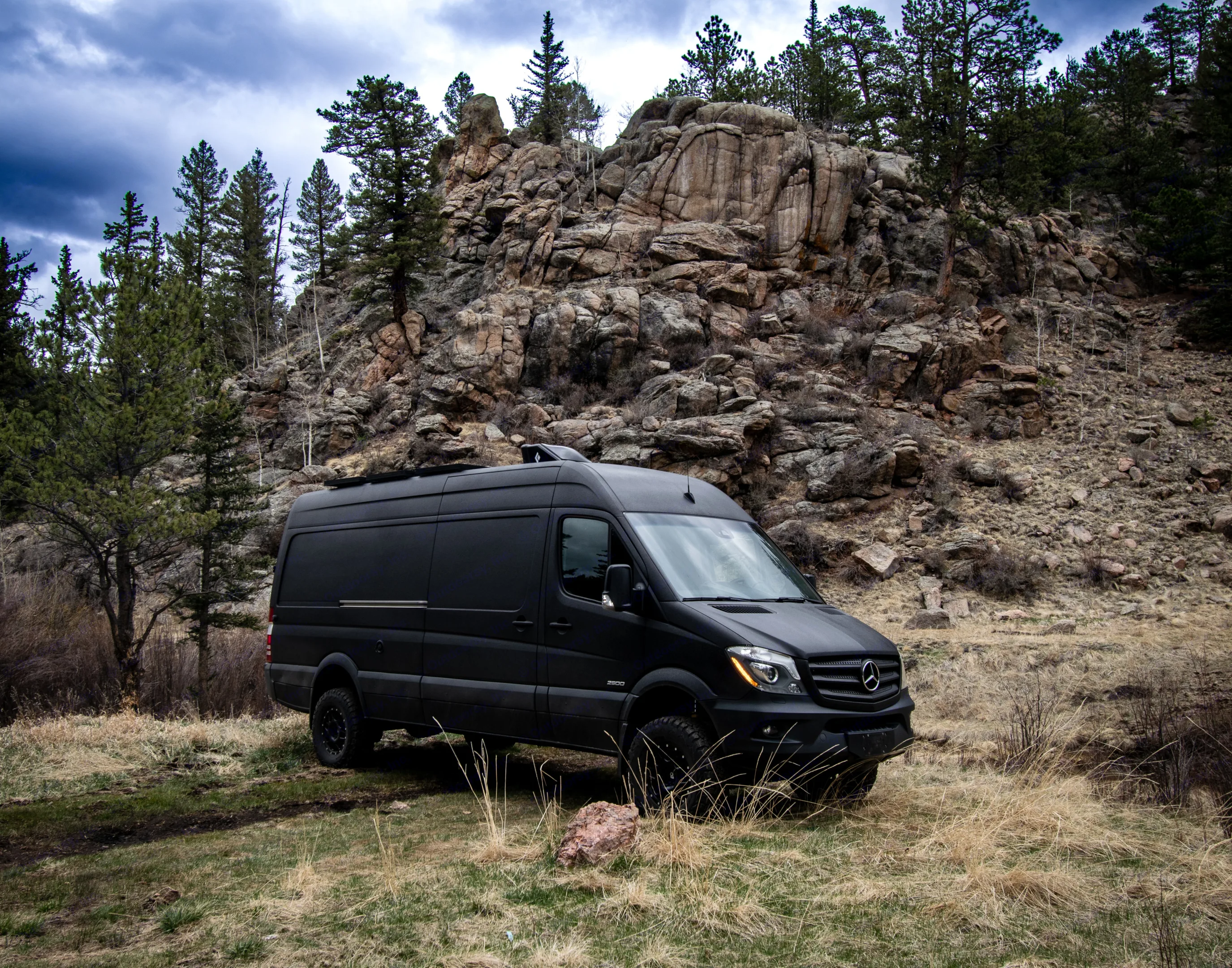 Black Sprinter van RV rental parked in rugged mountain landscape with trees & rocky hills under a. Mercedes-Benz Sprinter 2500 2016