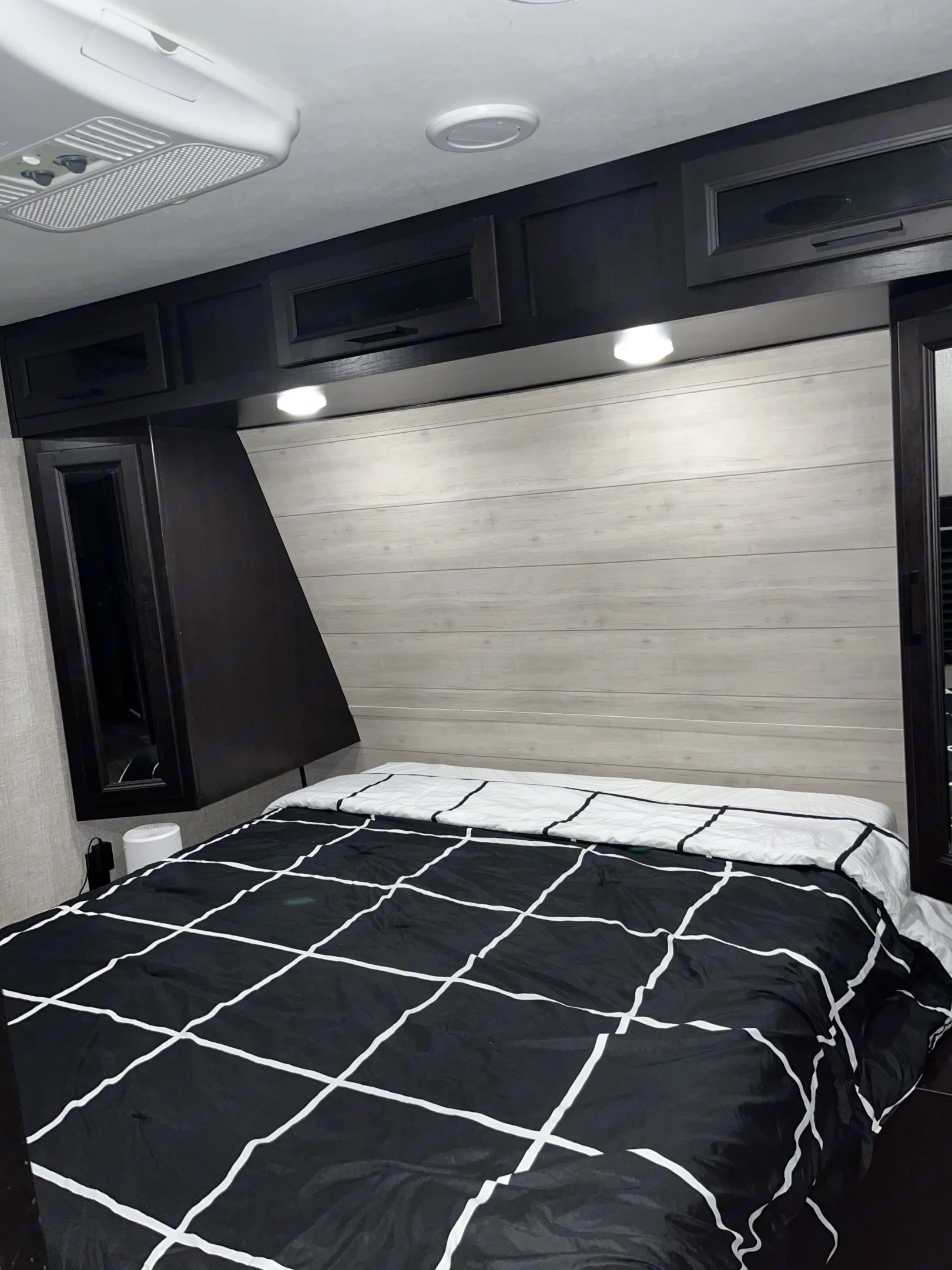Cozy RV rental bedroom featuring a modern black & white bed, wood-paneled headboard, and overhead storage for. Jayco Jay Flight 2022